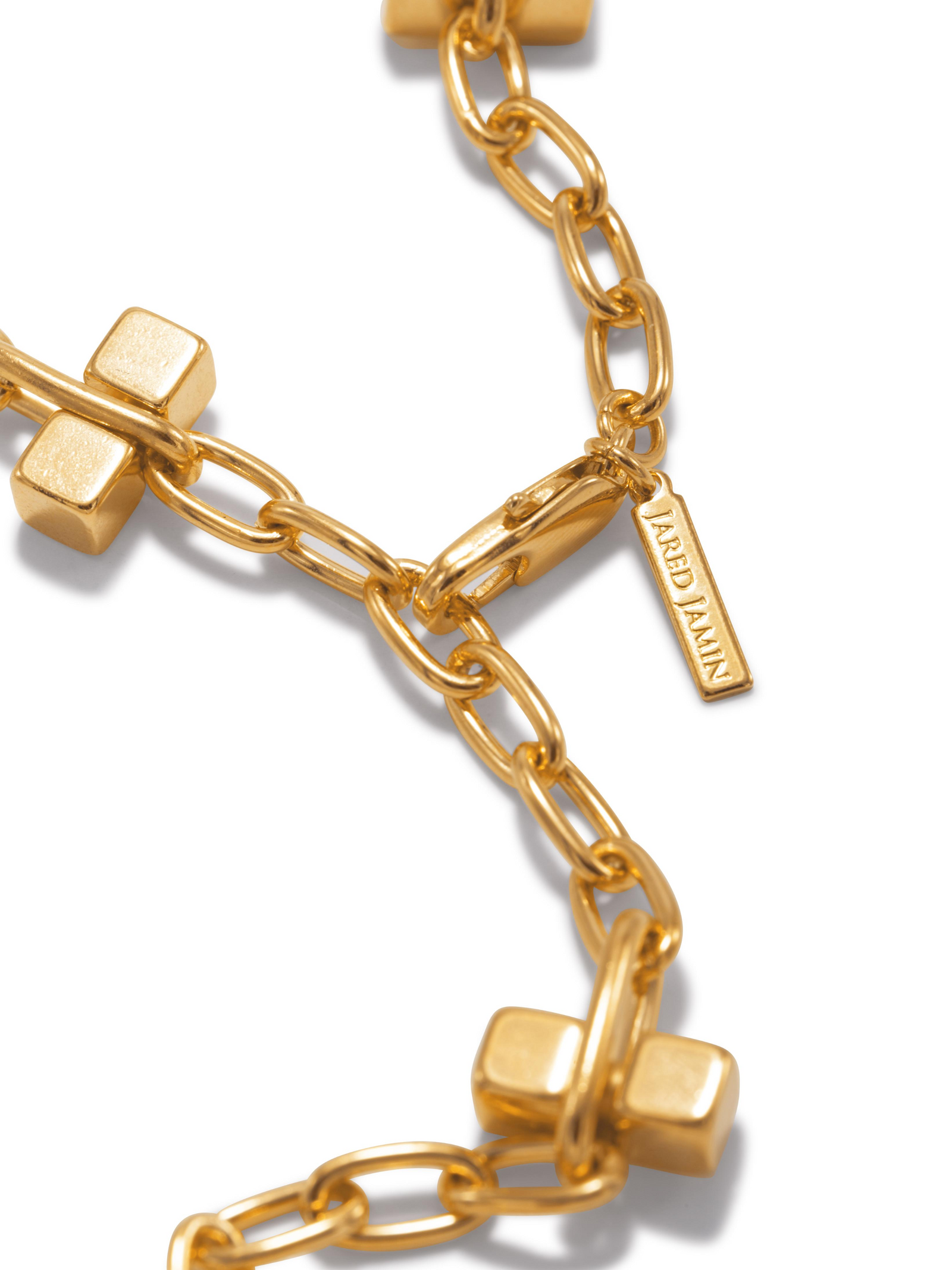 Close-up of a gold chain necklace with rectangular links and cube accents. A small rectangular tag is attached, engraved with the text "ARREDAIN." The background is plain white.