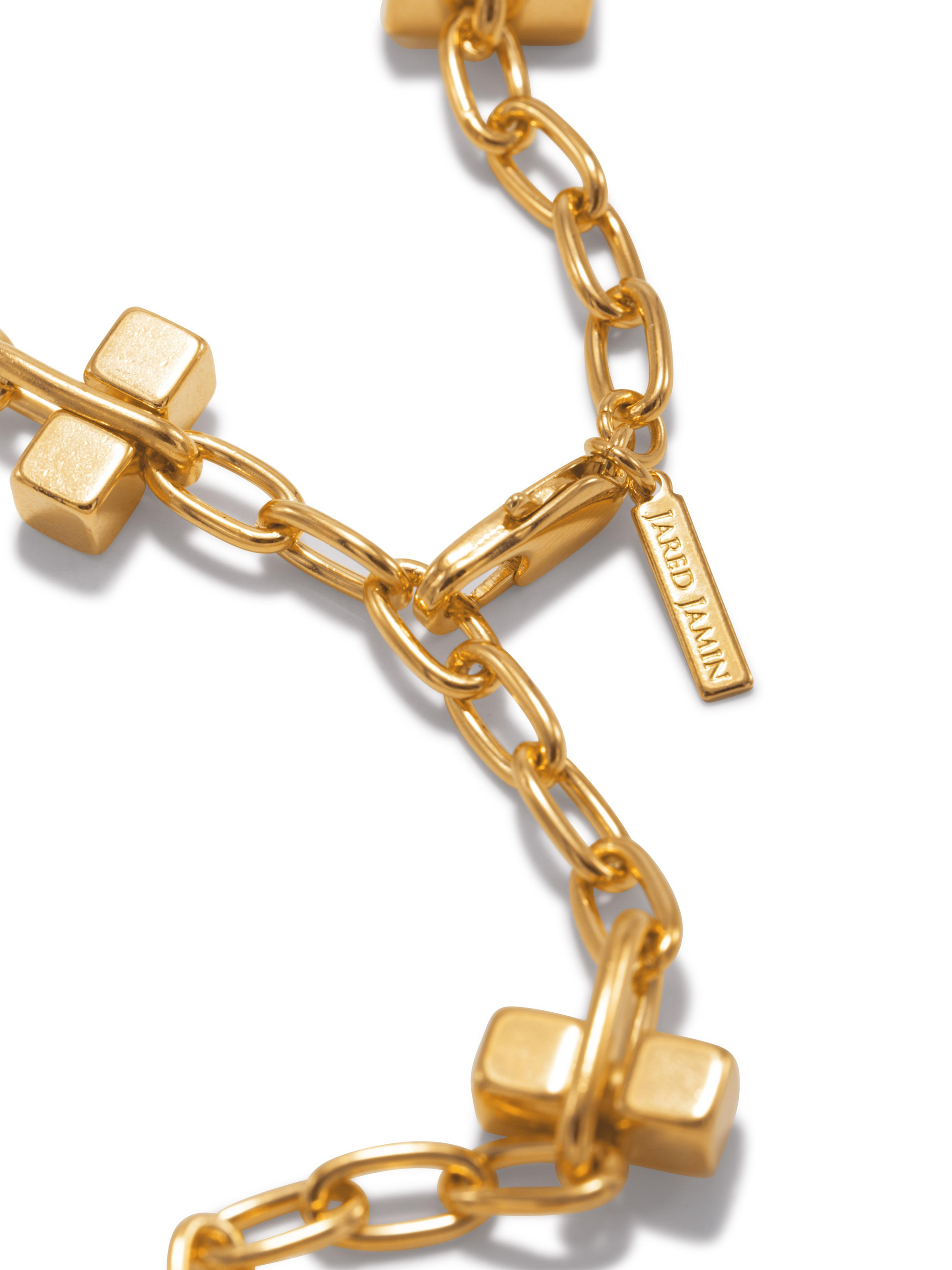 Close-up of a gold chain necklace with rectangular links and cube accents. A small rectangular tag is attached, engraved with the text "ARREDAIN." The background is plain white.