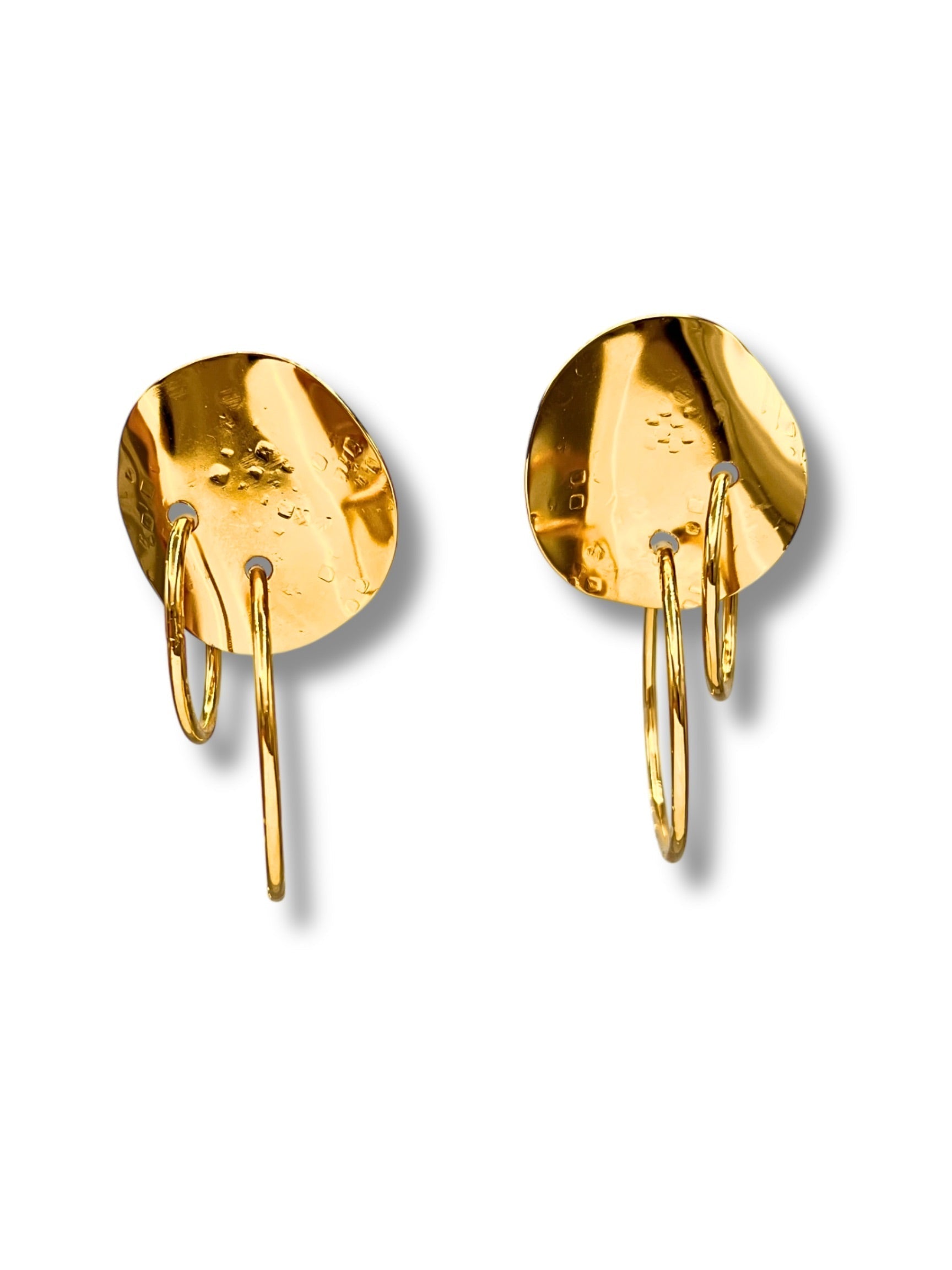 Elegant gold earrings featuring a textured circular disc with two interlocking hoops hanging below, casting soft shadows on a white background.