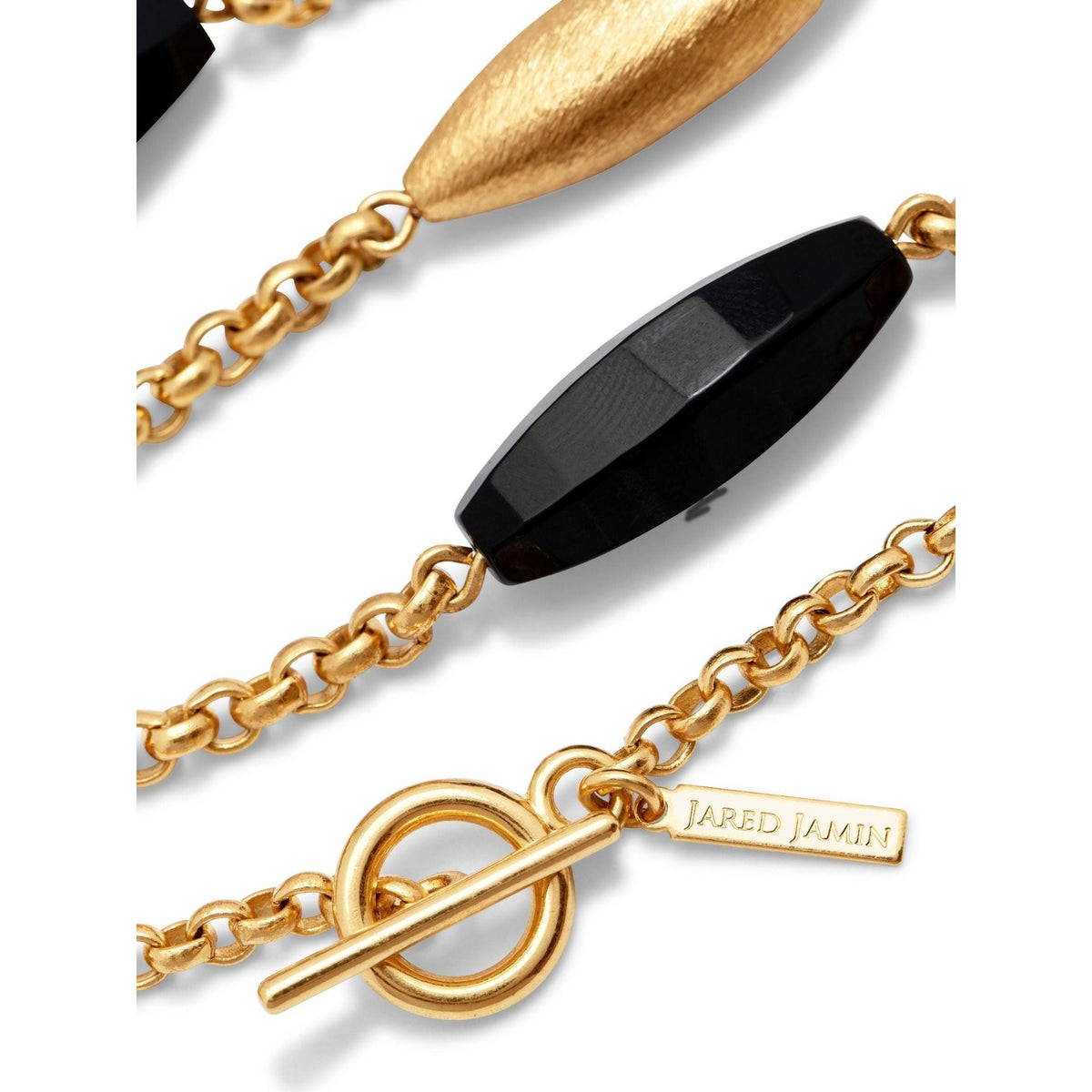 primer plano of the Zeppelin Luna Onyx collar de JAREDJAMIN Joyería Online, con faceted black beads, an elongated mate 18k oro bead, toggle clasp, y a rectangular oro "Jared Jamin" tag, set against a fondo blanco.