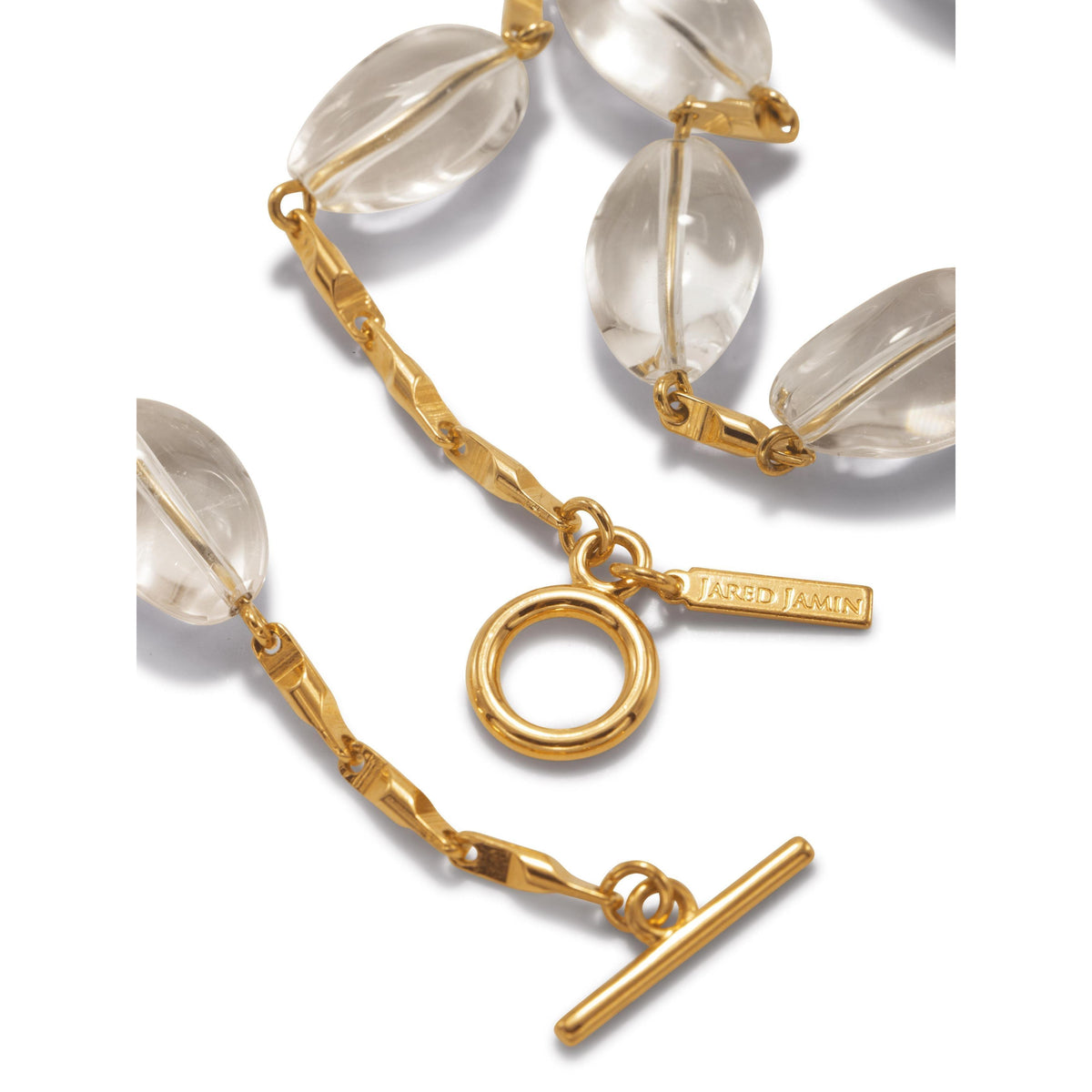 Un primer plano of the Arctic oro Bar-Link collar de JAREDJAMIN Joyería Online, con large oval cristal Quartz beads linked con texturizado oro hardware y an 18K oro Plated toggle clasp engraved con "JARED JAMIN.