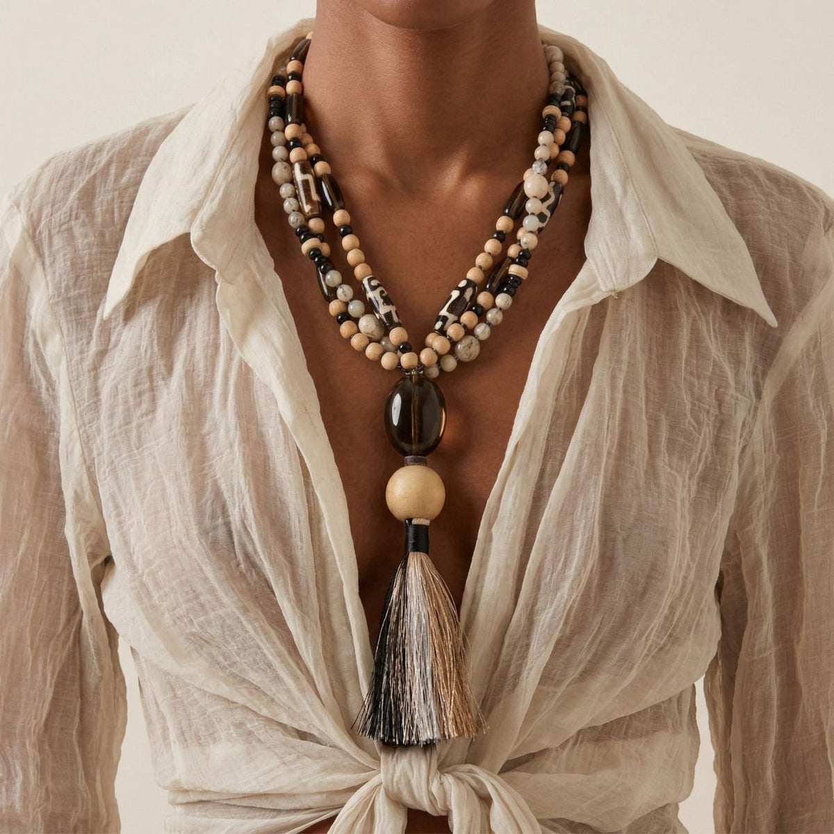 Side-angled model view of the Adamah Necklace, showcasing how the triple-strand beads drape and the movement of the multi-tonal sand and charcoal tassel.