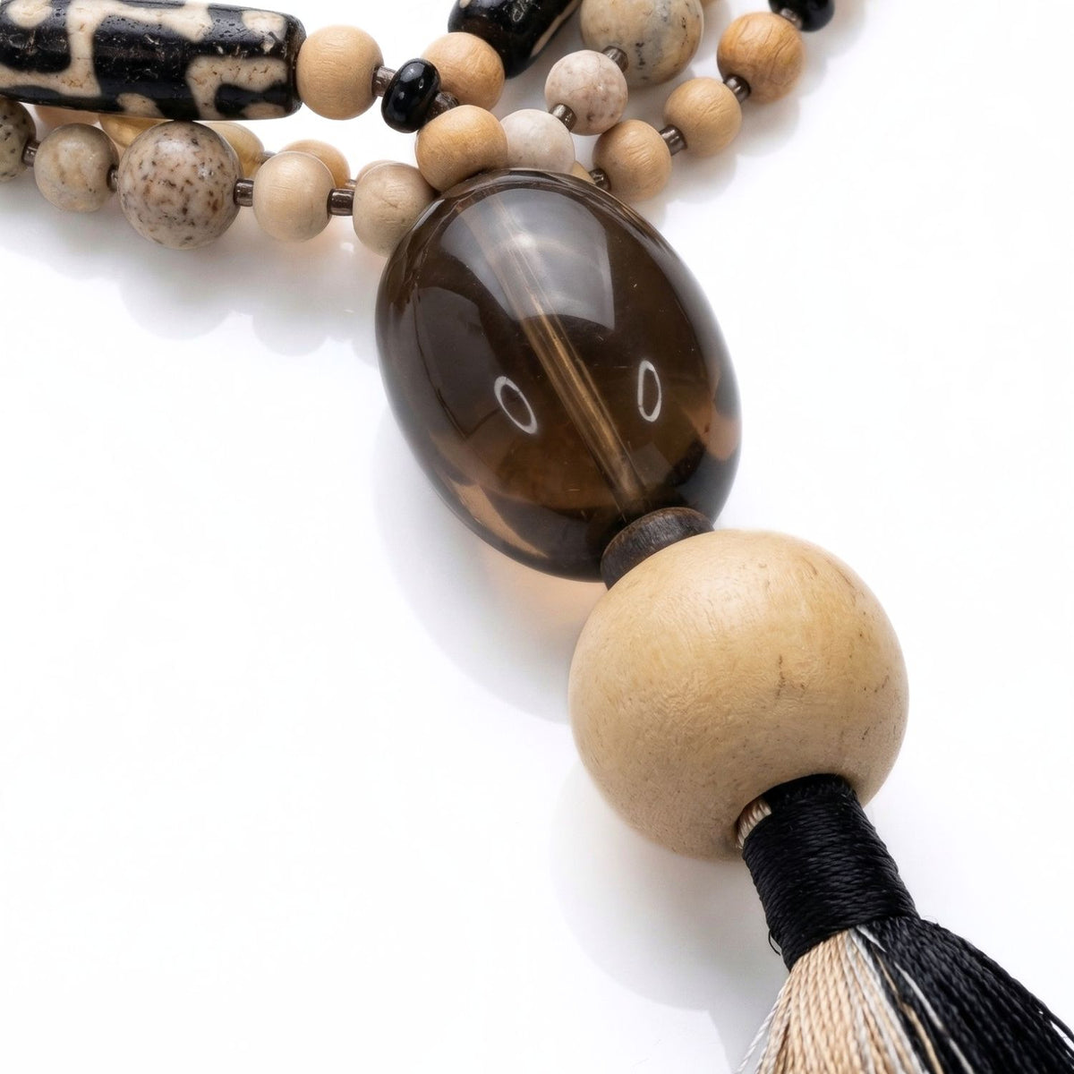 Close-up detail of the Adamah focal point: a large pebble-smooth Smoky Quartz gemstone, a blonde wood sphere, and the intricate metallic seed bead segmentation.