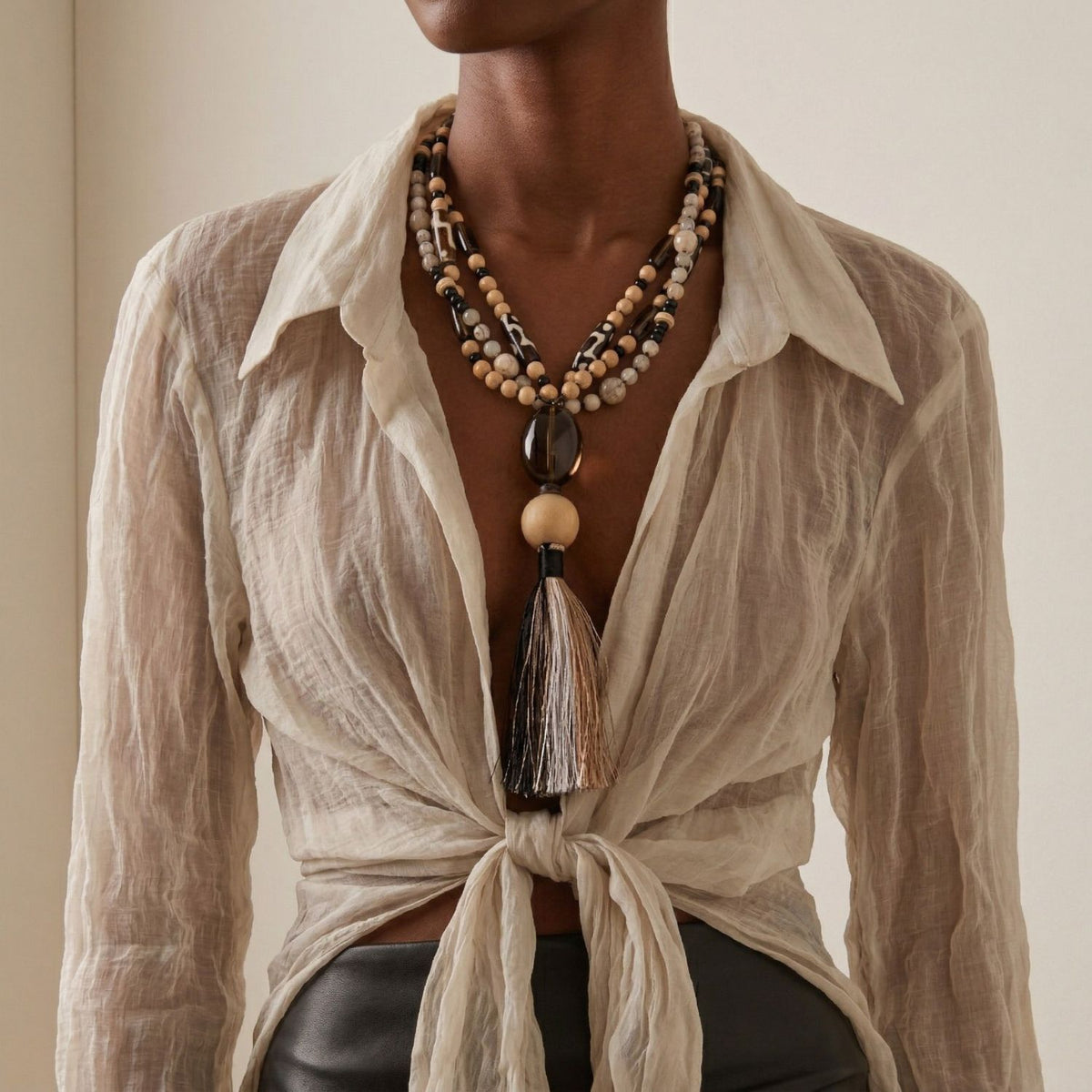 Lifestyle view of the Adamah Beaded Tassel Necklace worn with a sheer white blouse, highlighting its 20-inch length and architectural "Y" silhouette.