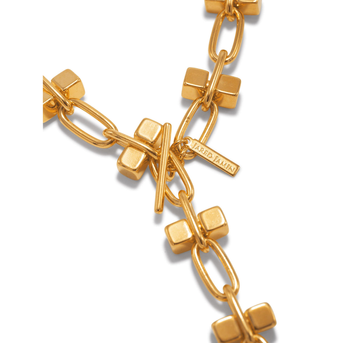 A close-up of the Blockbuster Gold Chain Long Necklace by JAREDJAMIN Jewelry Online shows chunky rectangular links, square beads, a toggle clasp, and a rectangular tag engraved with "JARED JAMIN" near the highly polished closure.