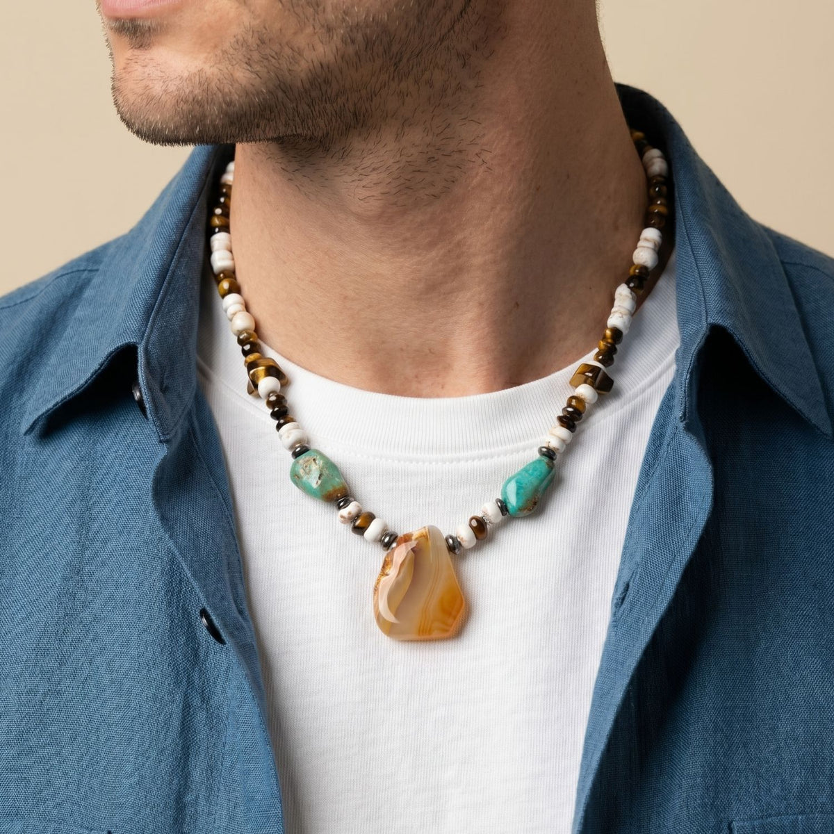 Studio style portrait showcasing the 19-inch Badlands mineral pendant necklace styled on a model with an open linen resort shirt, demonstrating its masculine scale and natural stone color blocking.
