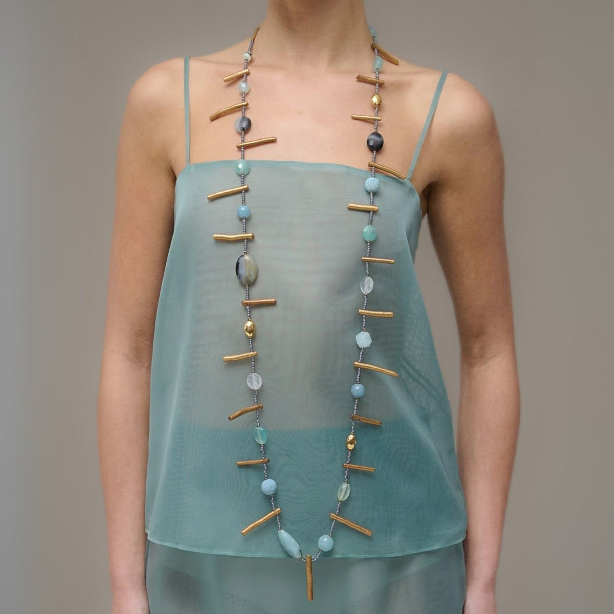 Los Beach Dunes Long collar de JAREDJAMIN Joyería Online, con blue y oro 18K bañado en oro beads, matted hematite, y oro tube accents, worn con a sheer light teal spaghetti-strap top against a neutral background.