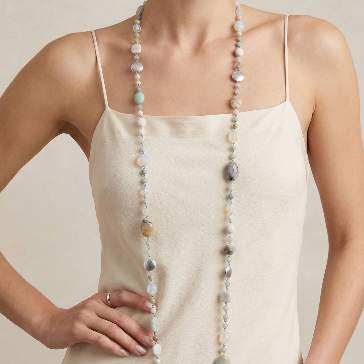 Mid-shot studio angle of a model showcasing the Nerissa wire-linked strand resting against a cream silk camisole, highlighting the individual textures of the aquamarines, opals, and silver-plated copper discs.