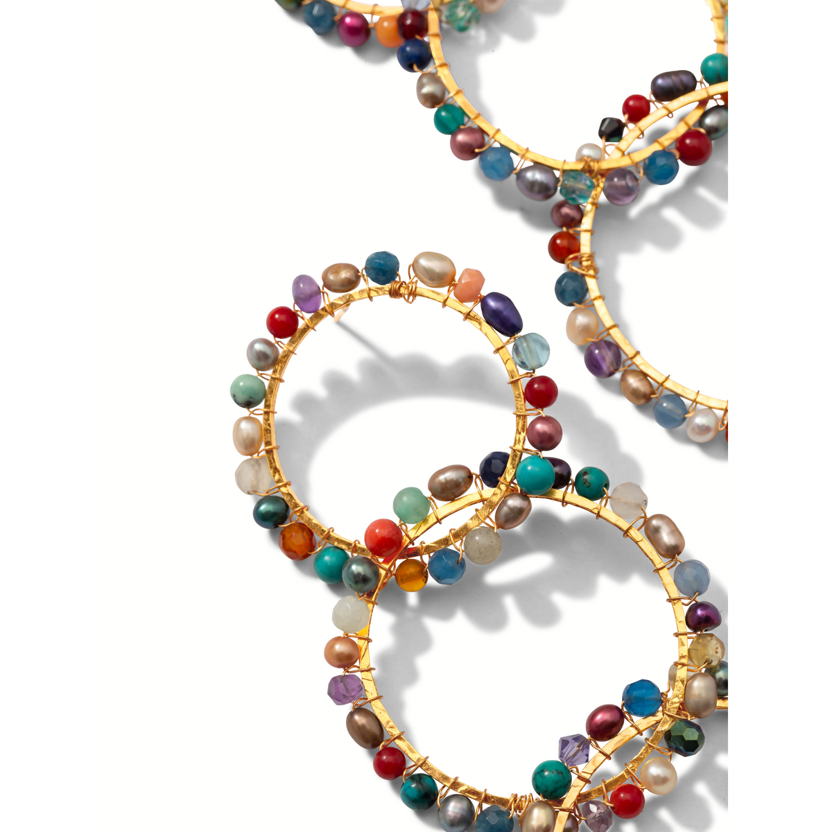 Four Begemmed Lindy 18K or Plated boucles d'oreilles de JAREDJAMIN Bijoux en Ligne overlap sur un fond blanc, each decorated avec colorful, irregular gemstones et beads in red, blue, green, purple, orange, et perle hues. Shadows fall right.