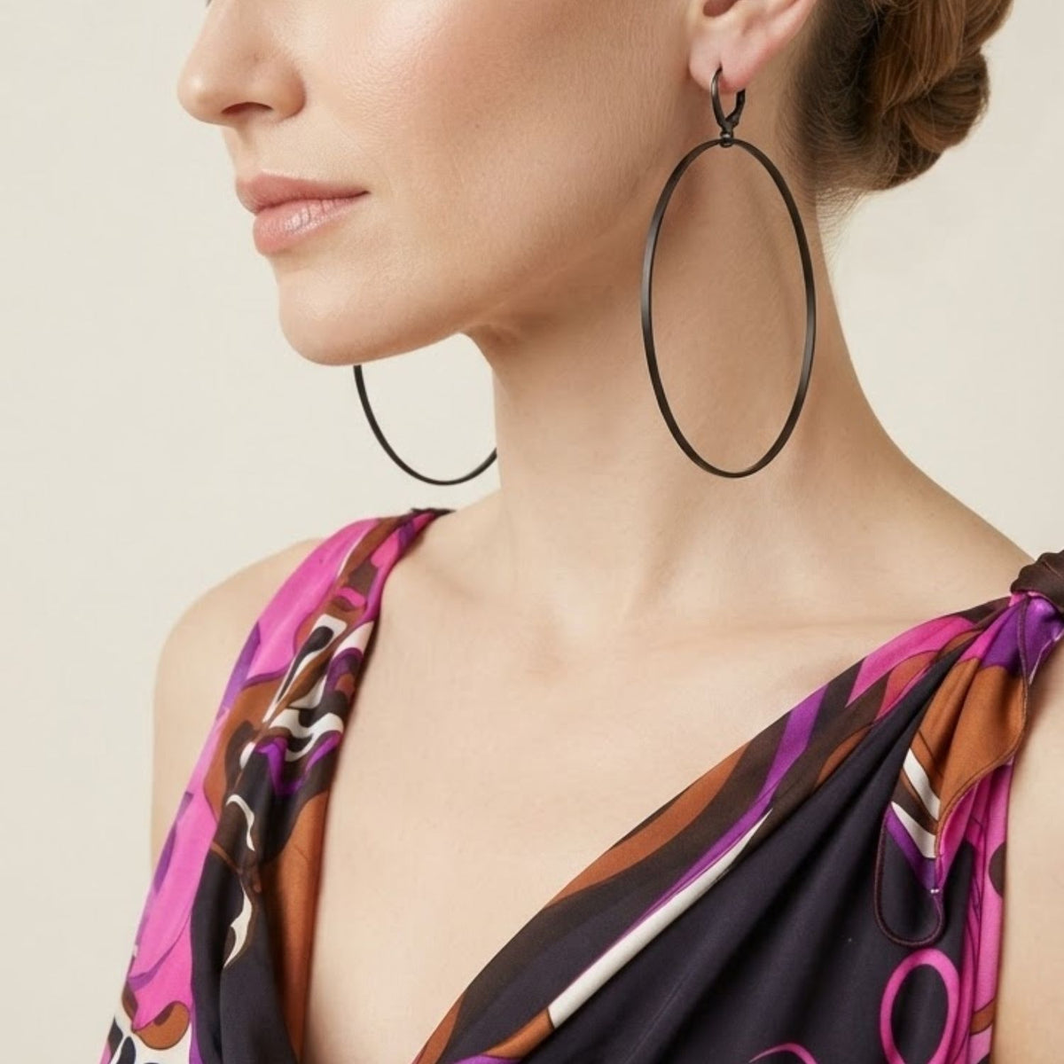 Side profile view of a model wearing the 3.75-inch Nyx Black Halo Hoop Earring, illustrating its dramatic scale and minimalist graphic silhouette styled against a pink and brown patterned dress.