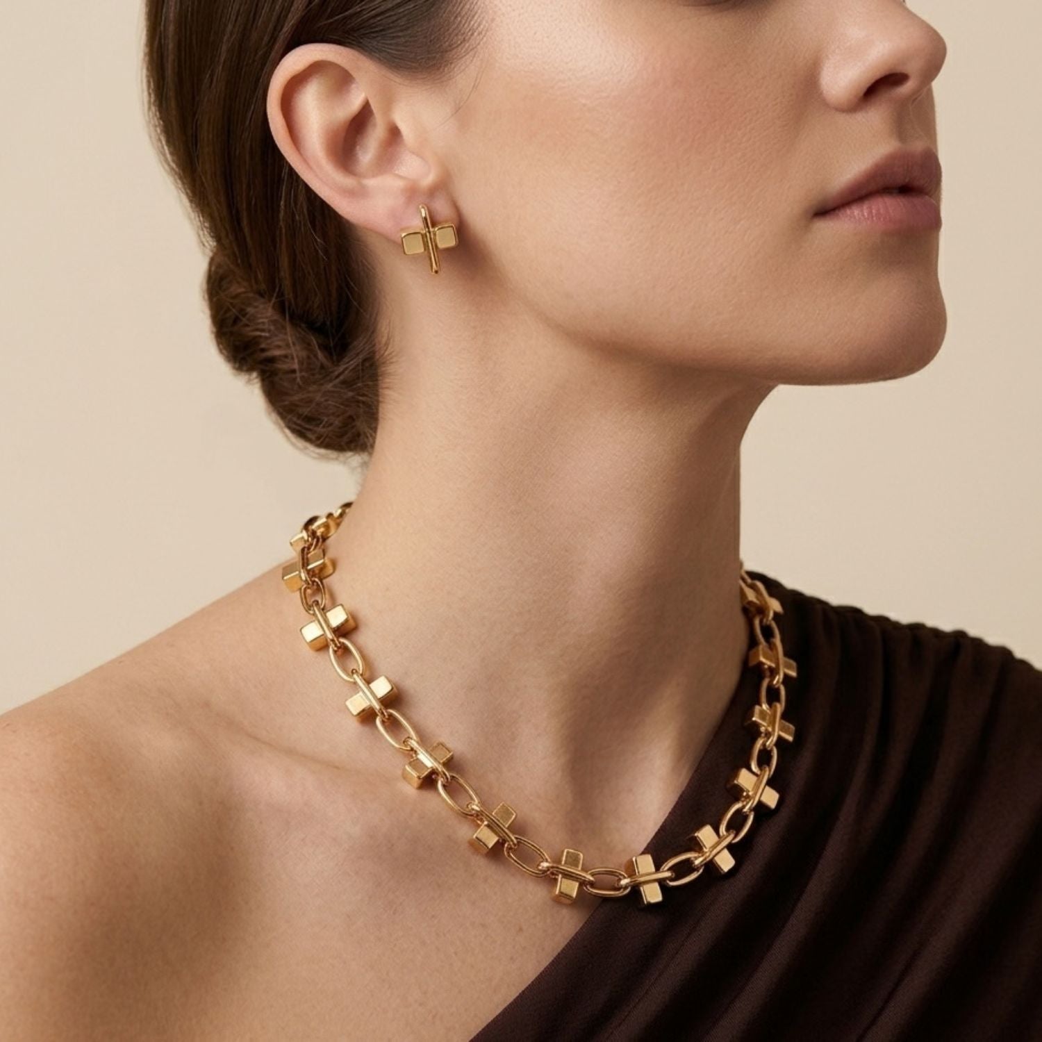 Isolated view of the JAREDJAMIN Gold Blockbuster Stud Post Earrings resting on a white surface, casting a soft shadow that highlights the intersecting 18k gold-plated cube and oval link design.
