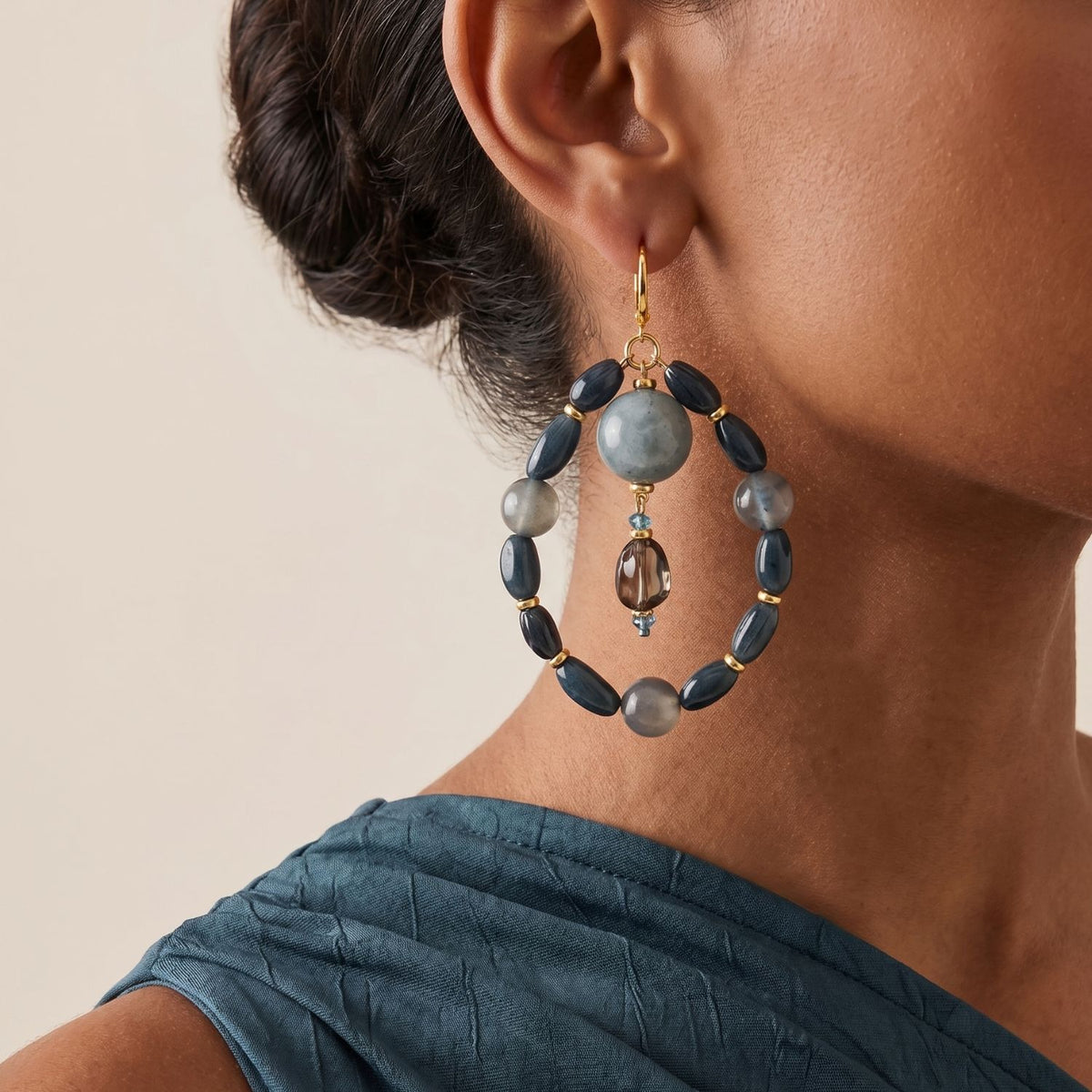 Side profile portrait view of a model wearing the 4-inch Blue Bean Agate and Crystal Statement Hoops, illustrating their architectural scale, floating central drop configuration, and deep blue color blocking styled with a draped teal top.