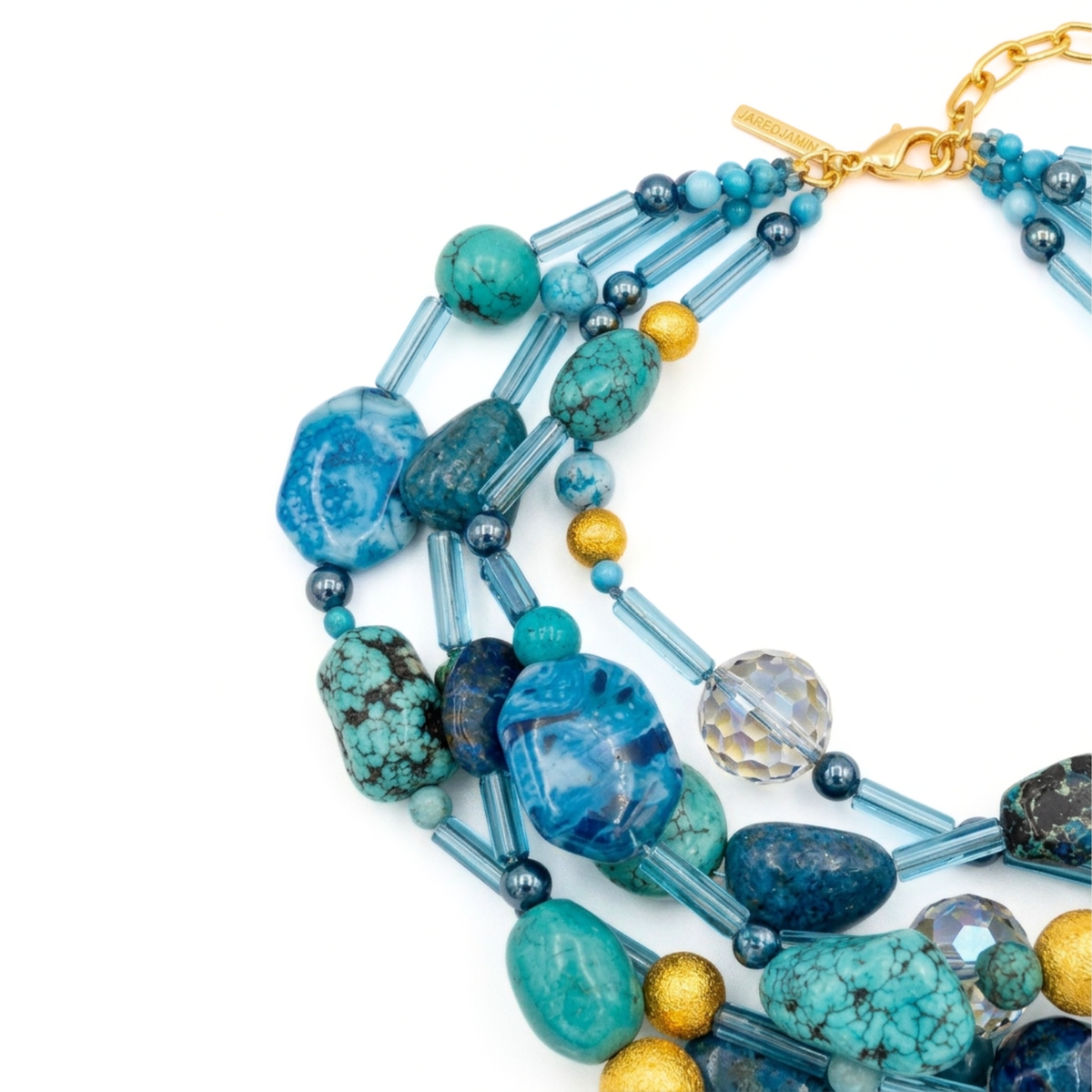 Angled studio layflat shot showing the layered strands, varying blue gemstones, and golden lobster clasp with extension chain of the Blue Reef statement necklace.