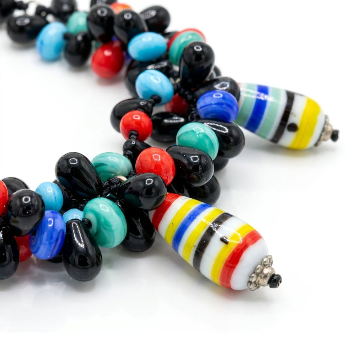 Sharp macro studio shot focusing tightly on the colorful striped vintage glass teardrop beads, the vibrant blue and red agate, and the textured black onyx base of the Candy Dandy statement necklace.
