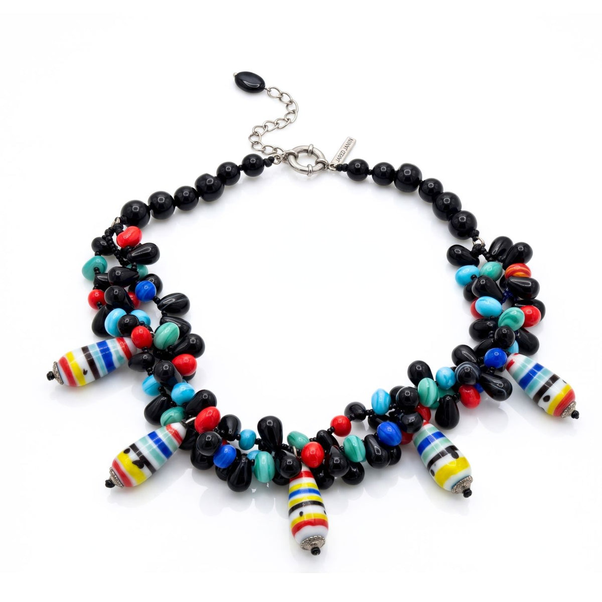 Angled, top-down flat lay shot of the JAREDJAMIN Candy Dandy Necklace resting on a white surface, showcasing the full circular drape, the colorful clustered gemstone drops, and the silver-toned extension chain and lobster clasp.
