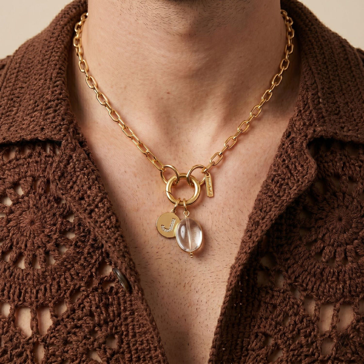A hand-assembled Clear Quartz Pebble Charm punctuates a chunky gold chain, refracting light atop a textured brown crochet shirt. Crafted in our West Hollywood studio in small, eco-conscious batches. Style Note: pivots from casual knits to after-dark tailoring.