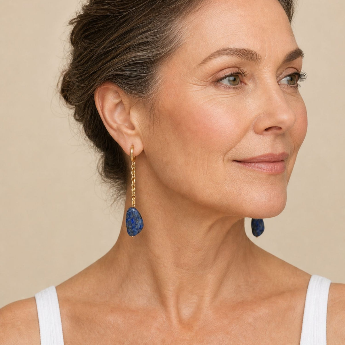 Close-up profile portrait of a female model wearing a white tank top and the 3.25-inch Cleo Lapis Lazuli Chain Drop Earrings, demonstrating their graceful drape, secure lever-back closure, and rich blue color against the skin.