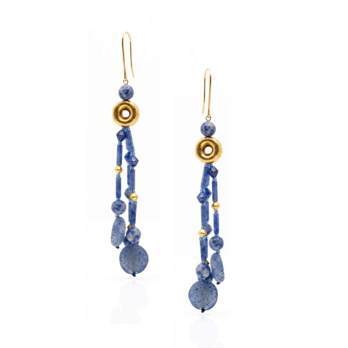 Angled layout view of the Celeste mineral drop earrings on a white surface, displaying the precise details of the round, tube, and rhombus sodalite beads alongside the brushed gold finish.