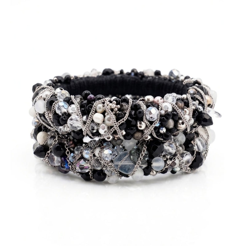 High-resolution, top-down flat lay photography shot with a Canon EOS 5D Mark IV macro lens, featuring the JAREDJAMIN Cocktail Clappers Bangle Set stacked on a white background to highlight the dense black, white, and gunmetal bead embroidery and woven silver chain.