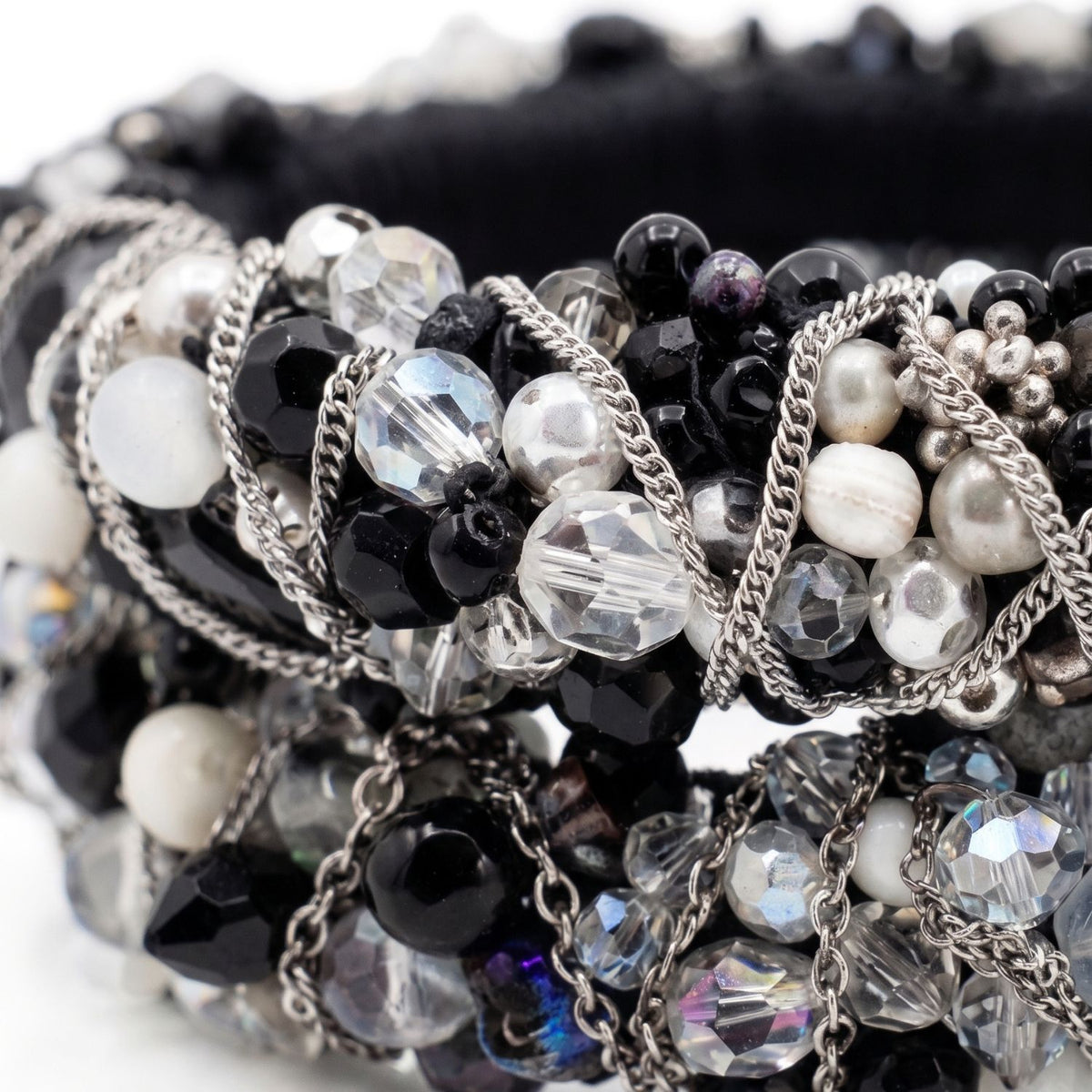 Sharp macro studio shot focusing tightly on the intricate hand-embroidery of the Cocktail Clappers Bangle Set, showcasing the tactile contrast between the black satin base, the milky white and black resin beads, and the thin silver metallic chain.