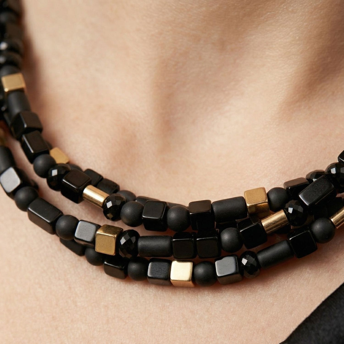 Close-up of the Corrinne necklace strands: matte and smooth onyx beads in varied shapes with small gold-plated hematite beads between them.