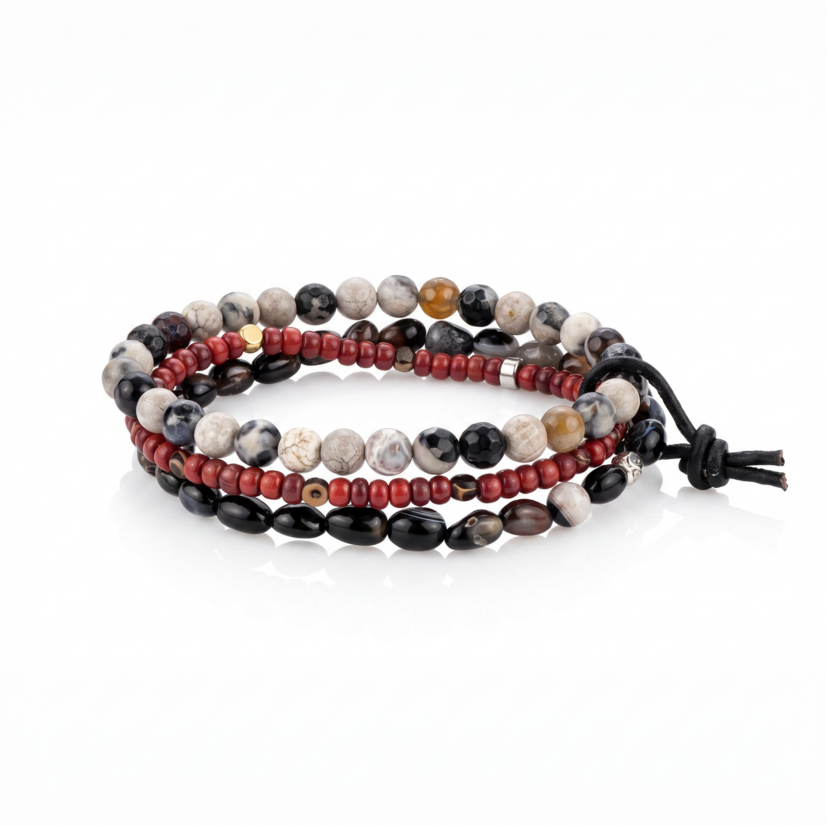 High-resolution studio product shot of the JAREDJAMIN Lucan Men's 3-Piece Stackable Bracelet Set displayed flat against a white background, highlighting the oxblood red glass, copper hematite, pebble agate, faceted jasper, and black leather tie.