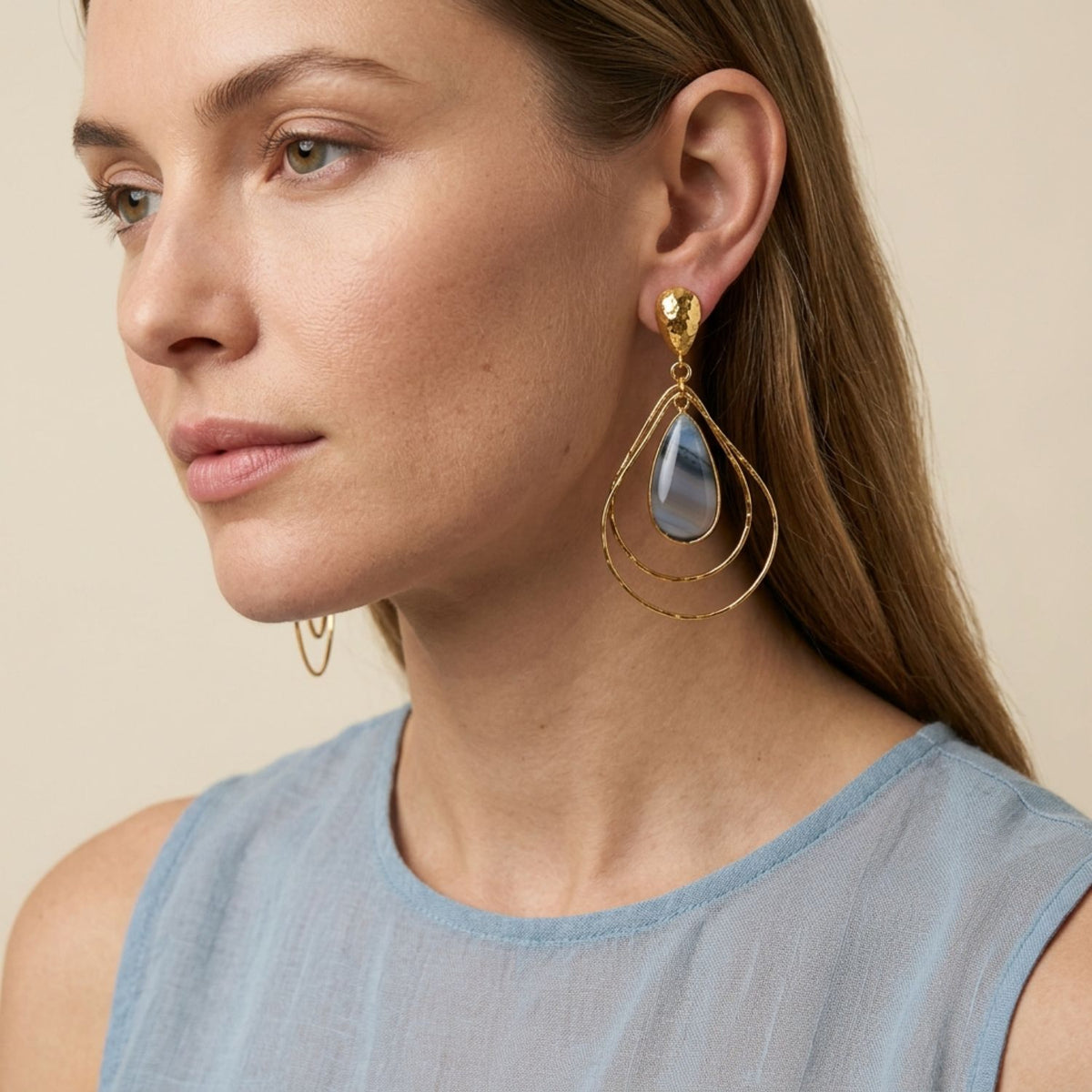 Side profile view of a model wearing the 3-inch Darlena Gold Banded Agate Earrings, demonstrating their architectural scale, nested geometry, and natural stone variance paired with a light blue top.
