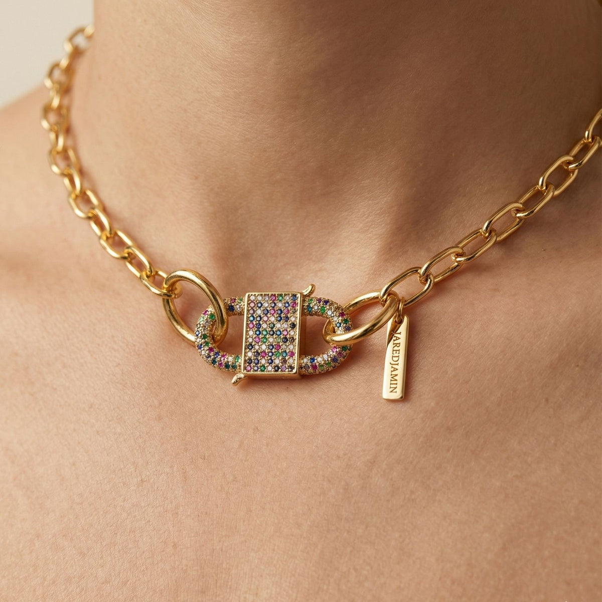 A close-up captures the Double Clasp Carabiner Multicolor necklace—an 18k gold, hand-assembled chunky chain crafted in our West Hollywood studio, with a prism-like rectangular clasp and NEEDJAWN tag. Small-batch. Eco-minded. Style note: transcends day to night.