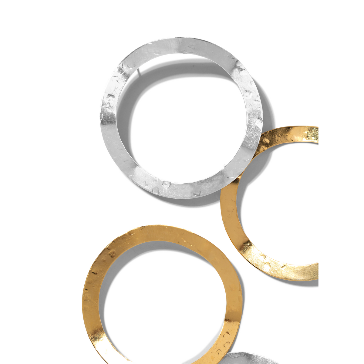Los Duet colgante Post pendientes de JAREDJAMIN Joyería Online presentan three texturizado metal anillos—one plata, y two 18K oro y plata Plated—overlapping sobre un fondo blanco, showcasing their tarnish-free surfaces con striking contrast y shadows.