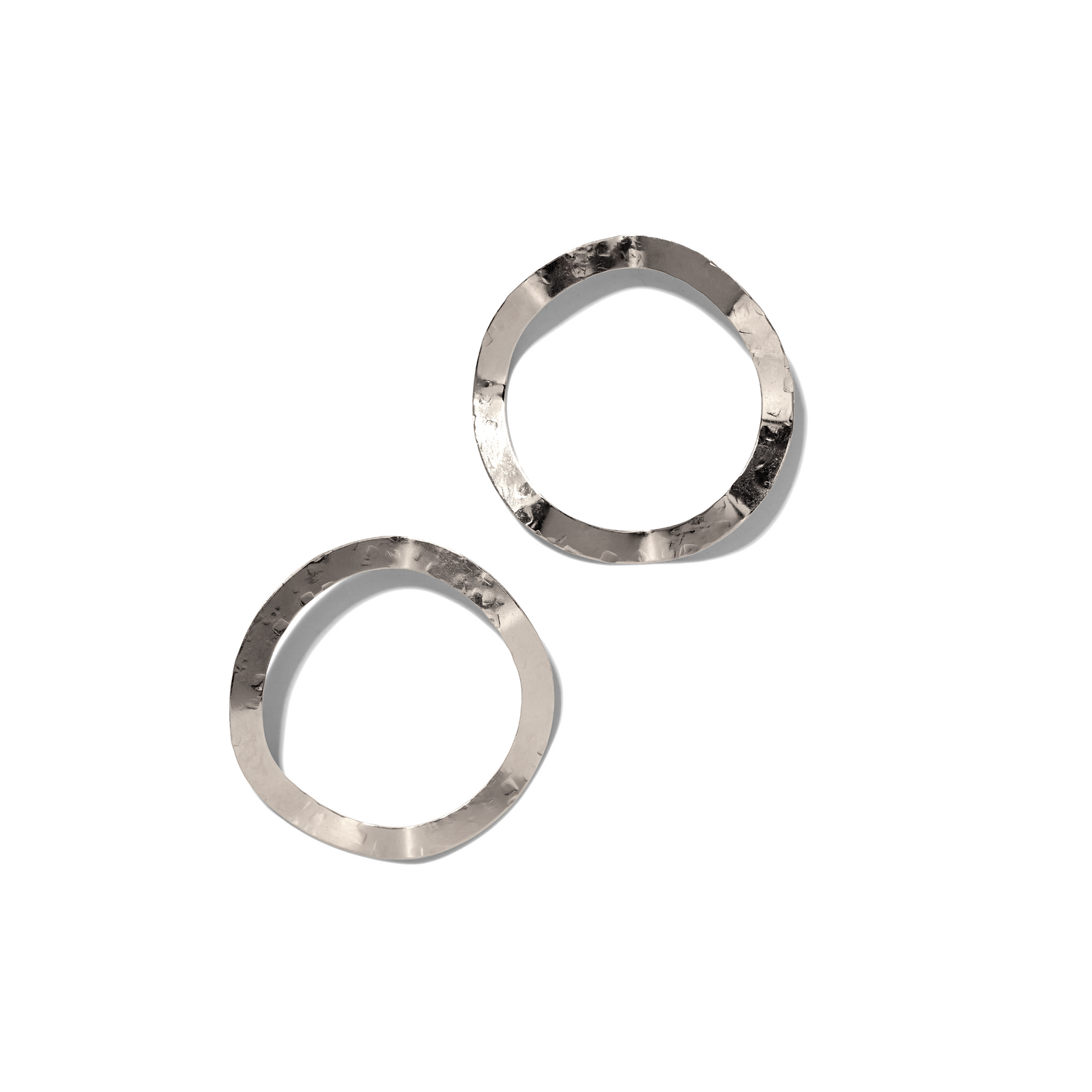 The Silver Duet Post Earrings by JAREDJAMIN Jewelry Online feature two organic, hammered silver forms with textured, reflective surfaces on a plain white background. Their artisanal, tarnish-free finish casts soft shadows to the lower right.