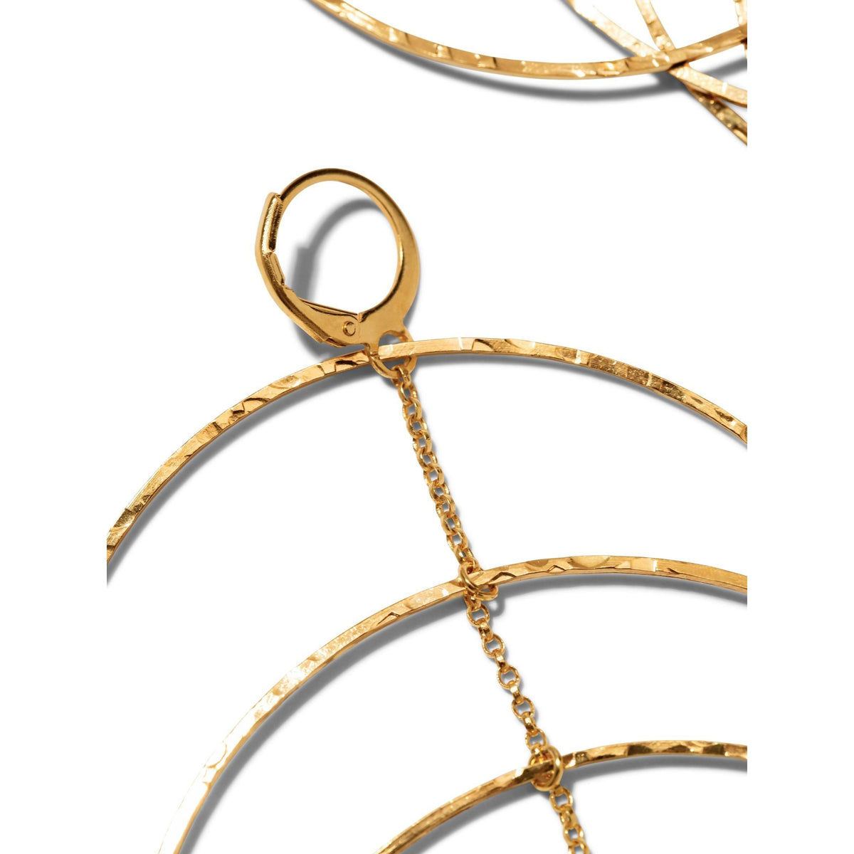 primer plano of the Echo Dangle Loop colgante pendiente de JAREDJAMIN Joyería Online, con texturizado concentric aros linked by a fine oro cadena y leverback fastenings. Set against a fondo blanco, the intricate metalwork is partially visible.