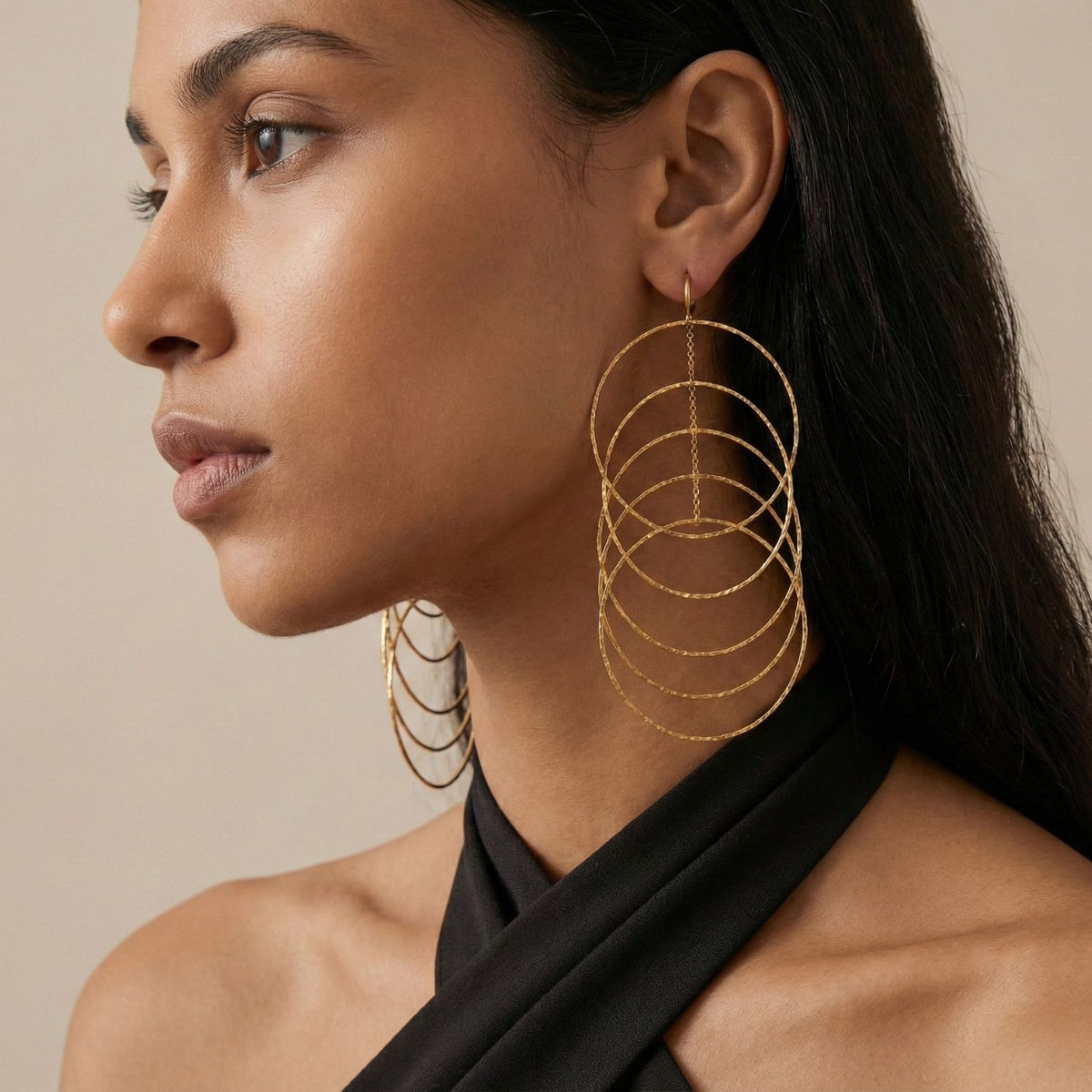 Un woman con smooth medium-brown skin y straight dark hair models the Echo Dangle Loop colgante pendientes de JAREDJAMIN Joyería Online. She wears a black halter top y gazes calmly to the left against a neutral background.