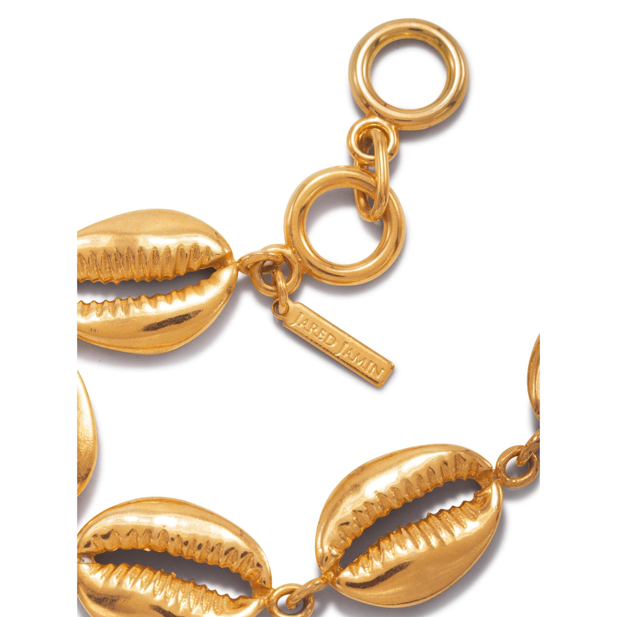 gros plan of the or Bel Mare Cowrie Seashell bracelet par JAREDJAMIN Bijoux en Ligne, crafted in 18K or plate. Un "JARED JAMIN" tag hangs near the clasp sur un fond blanc, highlighting its brillant finish.