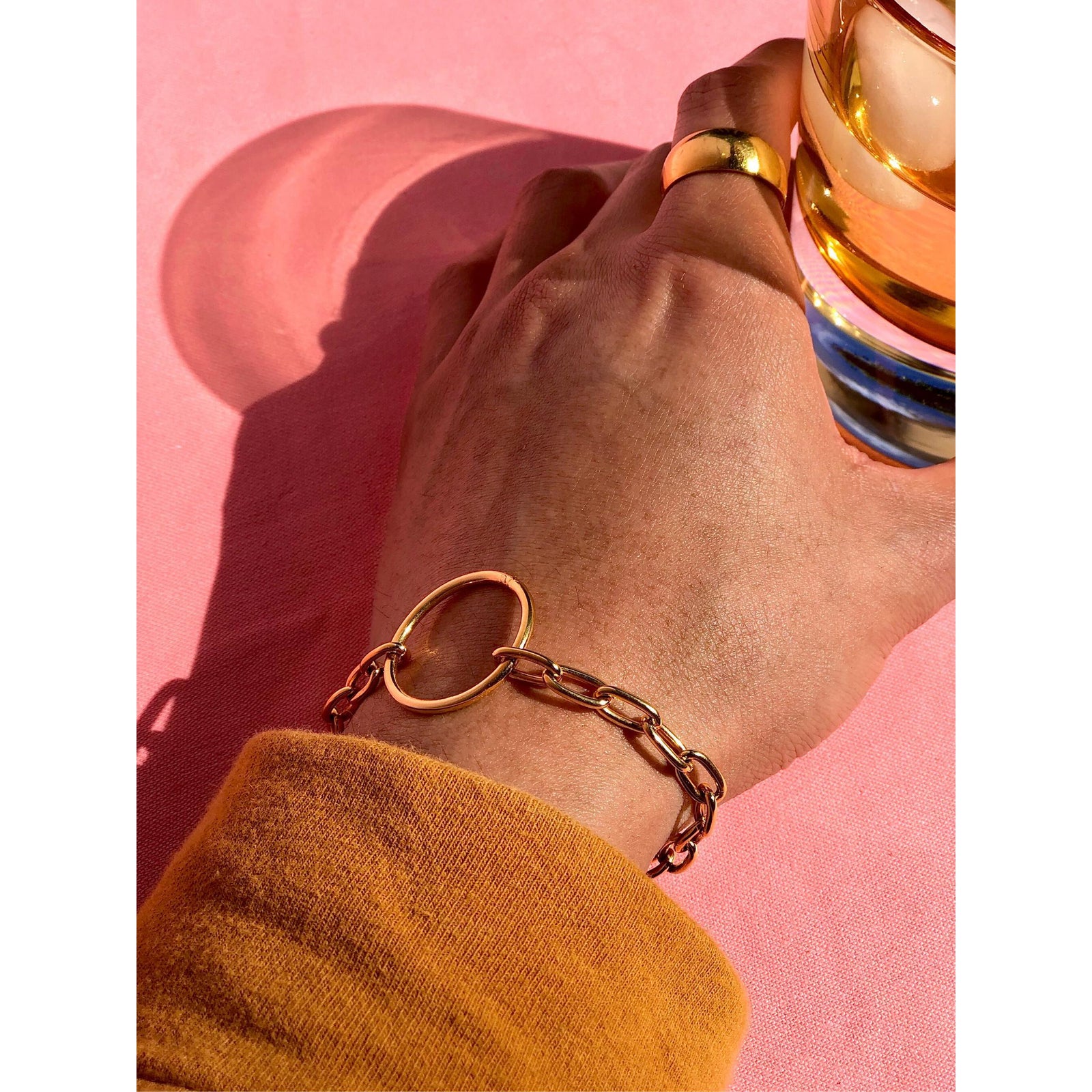The Gold Chain Reaction Ellipse Bracelet by JAREDJAMIN Jewelry Online features elongated links, a round open ring centerpiece, 18K gold plating, lobster clasp, and "PINKCITY" tag—styled flat on a white background.
