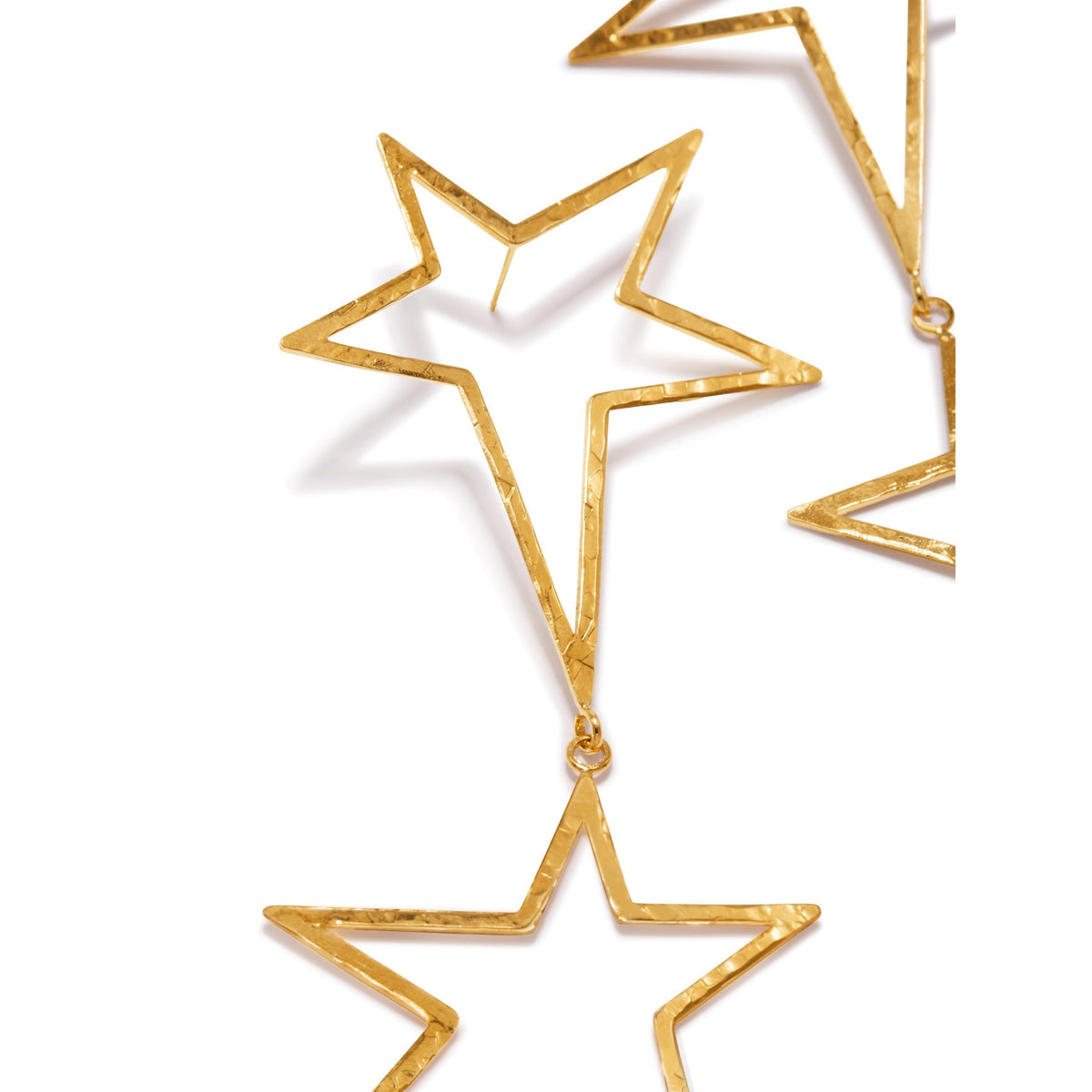 gros plan of or Shooting Star Dust Dangle Post boucles d'oreilles par JAREDJAMIN Bijoux en Ligne, avec two vertically linked, or-colored hammered metal hollow star outlines avec a texturé, reflective finish against a fond blanc.