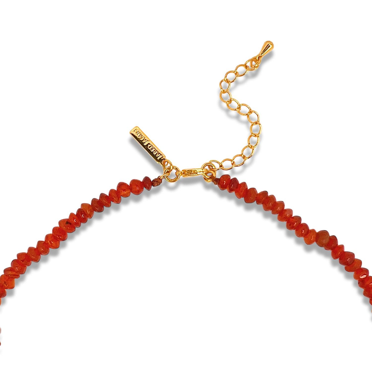 Close-up of the Gemstone Trail Carnelian Necklace by JAREDJAMIN Jewelry Online, showcasing small, irregular red stones and a gold-toned clasp with extender chain and rectangular brand tag, all set against a plain white background.