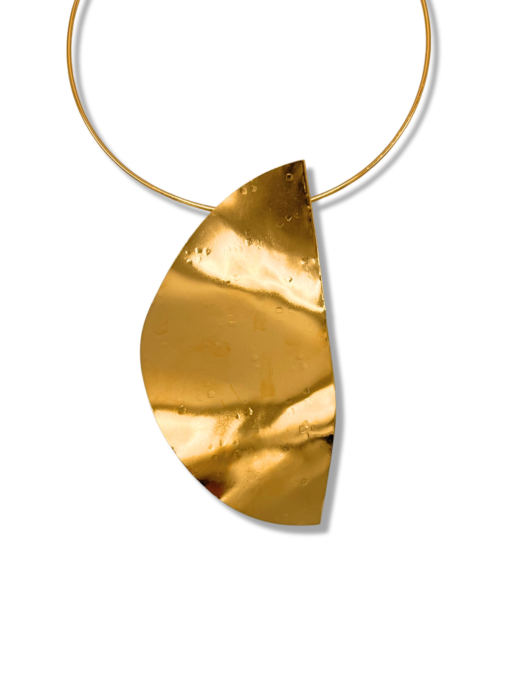 The Geo Twist Pendant Neck Wire from JAREDJAMIN Jewelry Online is an elegant gold choker with a wide band and adjustable clasp. It features an 18K hammered gold crescent pendant that adds subtle dimples and reflections.