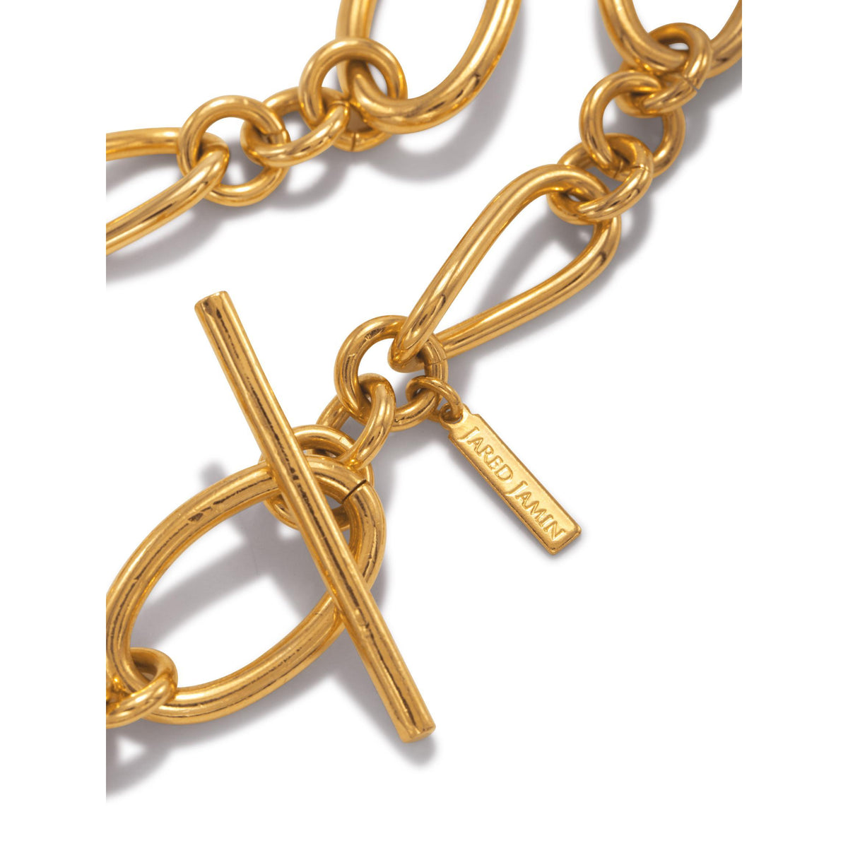 primer plano of the oro Ophelia cadena Toggle pulsera de JAREDJAMIN Joyería Online, con oval y round links, an 18K bañado en oro T-bar toggle clasp, y a branded tag, exhibido sobre a fondo blanco.