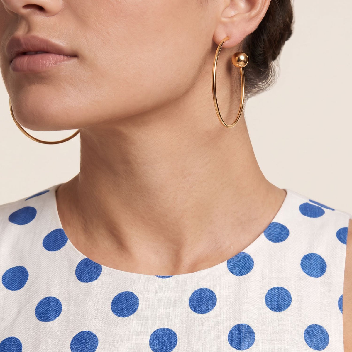 Side profile portrait of a model wearing the 3-inch Gold Orbita Comet hoop earring, showing its orbital drape and 13mm polished sphere resting along the jawline.