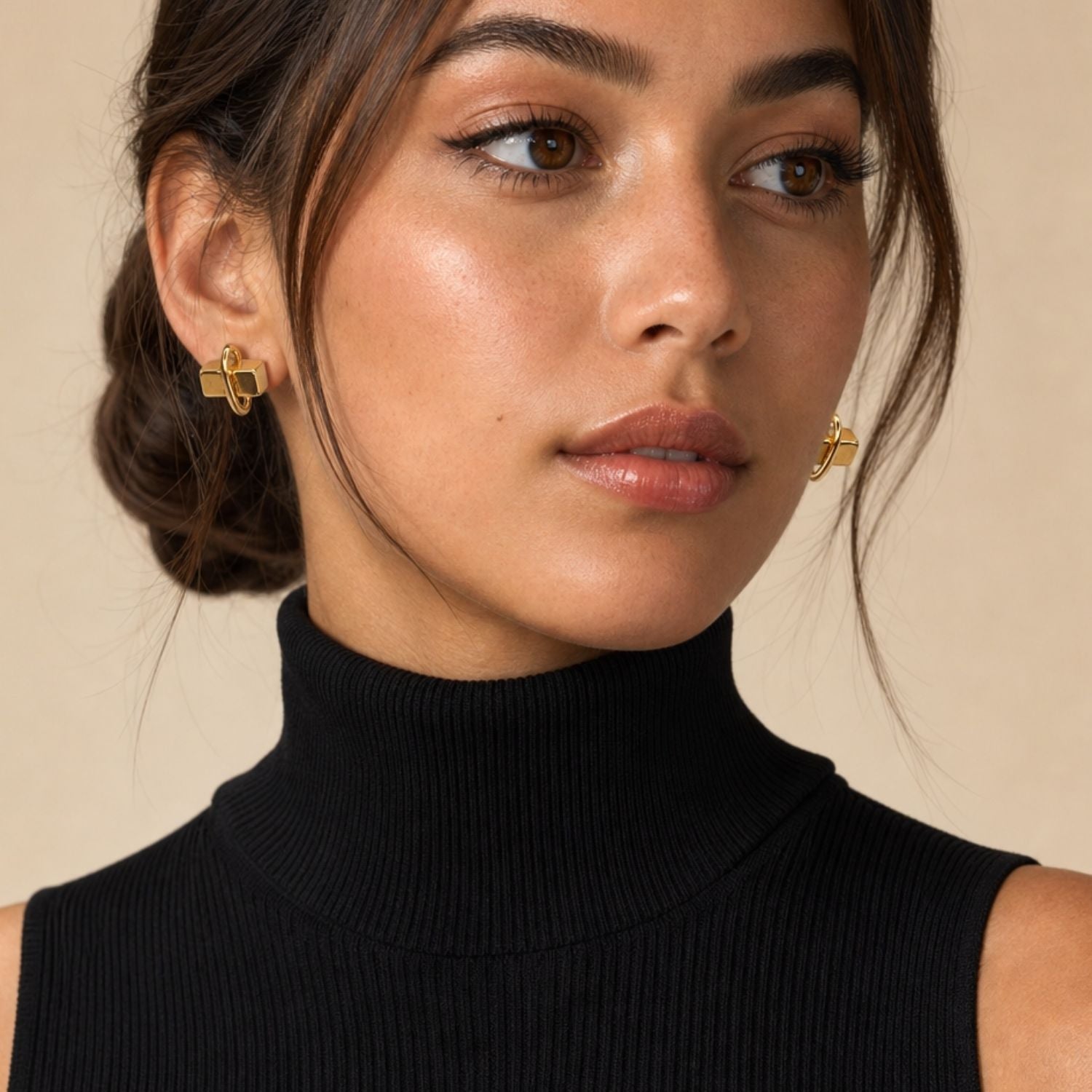Isolated view of the JAREDJAMIN Gold Blockbuster Stud Post Earrings resting on a white surface, casting a soft shadow that highlights the intersecting 18k gold-plated cube and oval link design.