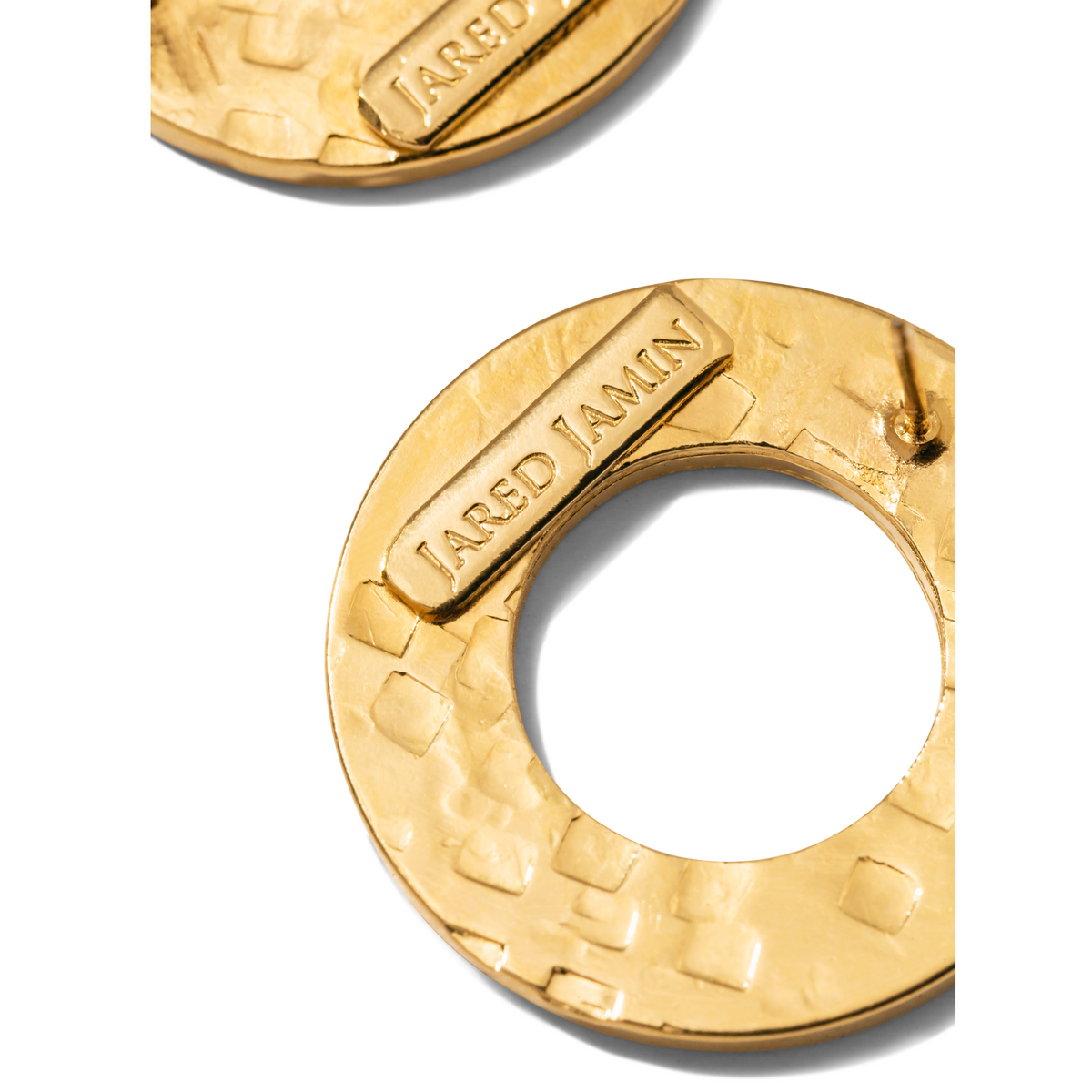 primer plano of two oro Colorado pendientes de JAREDJAMIN Joyería Online—texturizado, round 18K bañado en oro pieces con a hammered finish y rectangular plaques inscribed “JARED JAMIN.” One pendiente centered, the other partially visible on fondo blanco.