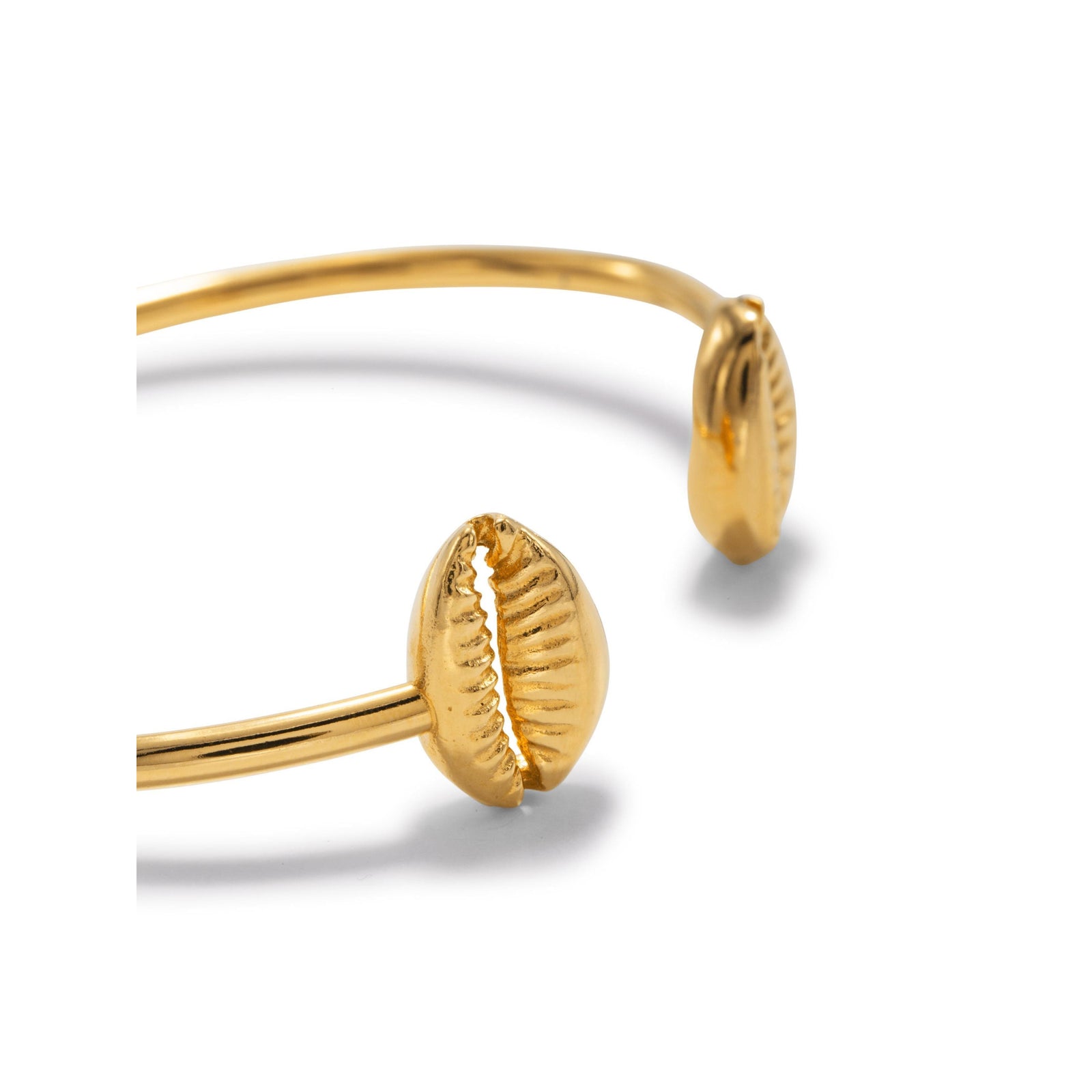 The Gold Cowrie Shell Cuff Bracelet from JAREDJAMIN Jewelry Online features an 18K gold, polished thin band with two cowrie shell-shaped ends for a textured, beach-inspired look.