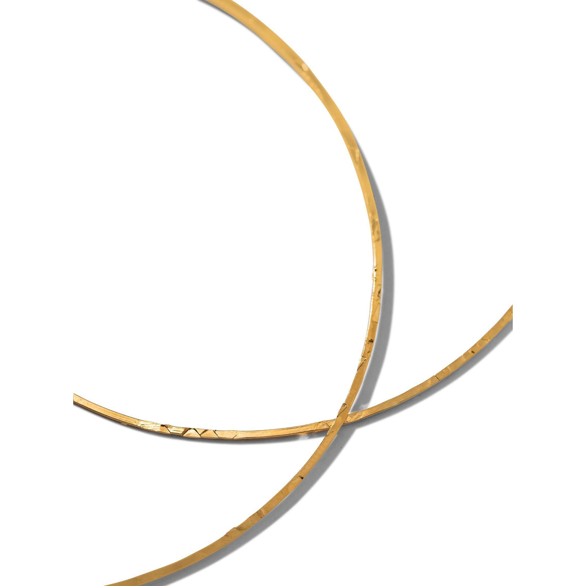 Two thin oro Halo texturizado aro pendientes de JAREDJAMIN Joyería Online overlap sobre un fondo blanco. Their metallic, texturizado surfaces are reflective, casting soft shadows that highlight the minimalistic elegance of the design.