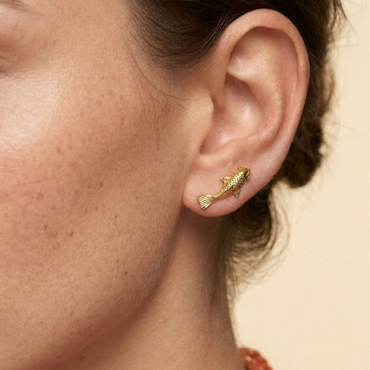 Side view profile of a model wearing the Playing-Koi gold fish ear climber, demonstrating how the 1-inch design climbs and curves elegantly up the ear lobe.