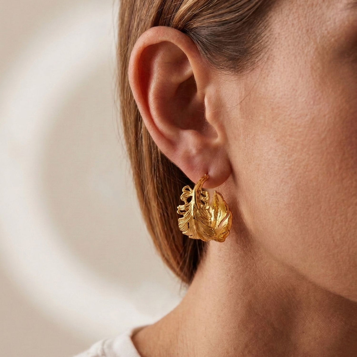 Model wearing the 1-inch Jared Jamin Gold Plume Hoops, demonstrating the secure post-back fit and how the textured feather design wraps elegantly around the ear.
