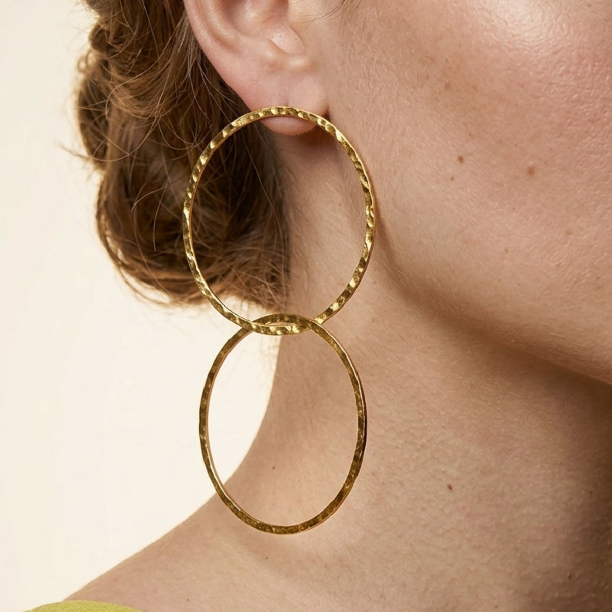 Close-up profile portrait of a female model's jawline, showcasing the fluid movement and scale of the double interlocking Gold Raquel Dangle Hoop earrings.