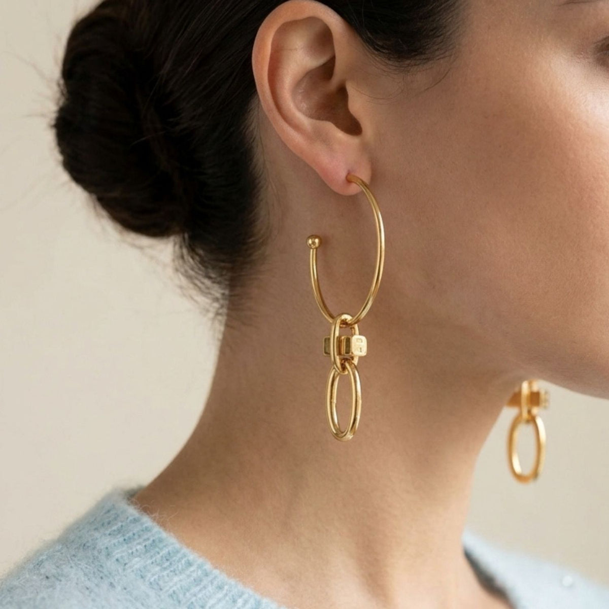 Profile portrait of a female model styling the 3.5-inch Gold Reign Hoop Earrings with the charms attached, highlighting the dramatic drop and geometric scale against her jawline.