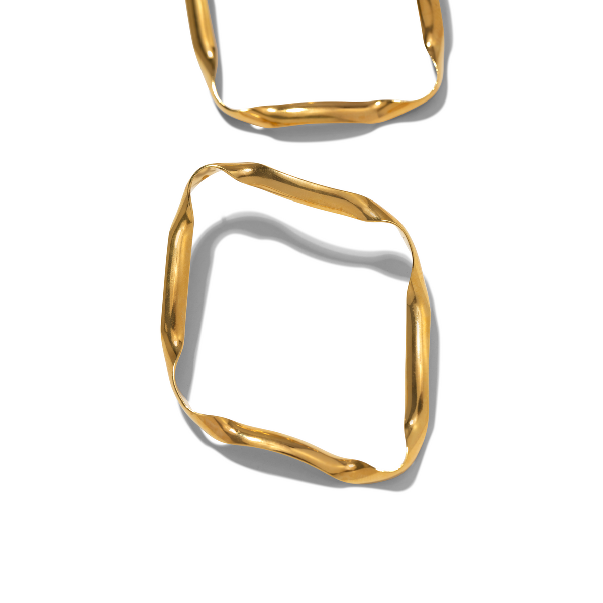 Un pair of oro Ribbonelle Post pendientes de JAREDJAMIN Joyería Online rest sobre un white surface, their brillante, subtly twisted 18K oro plating y irregular edges casting soft shadows para un minimal, modern effect.