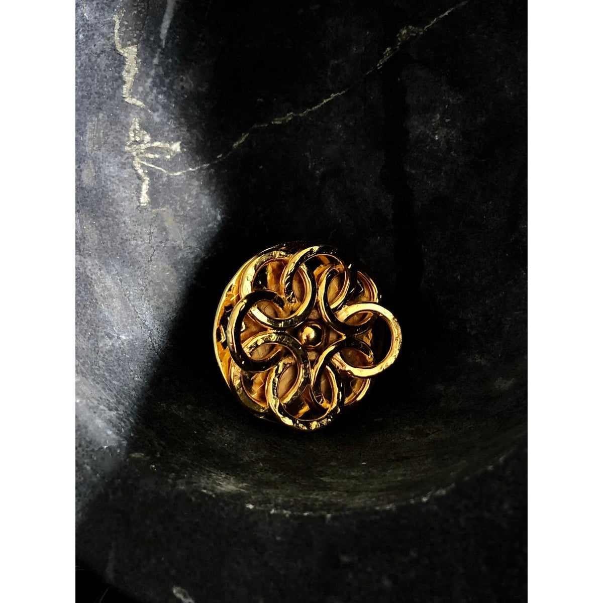 ゴールド Santorini Rose リング JAREDJAMIN製 ジュエリーオンライン, crafted in 18k ゴールド 付きの swirling knot design, shines against a dark, テクスチャード stone surface, its glossy ゴールド contrasting deep マット ブラック background.