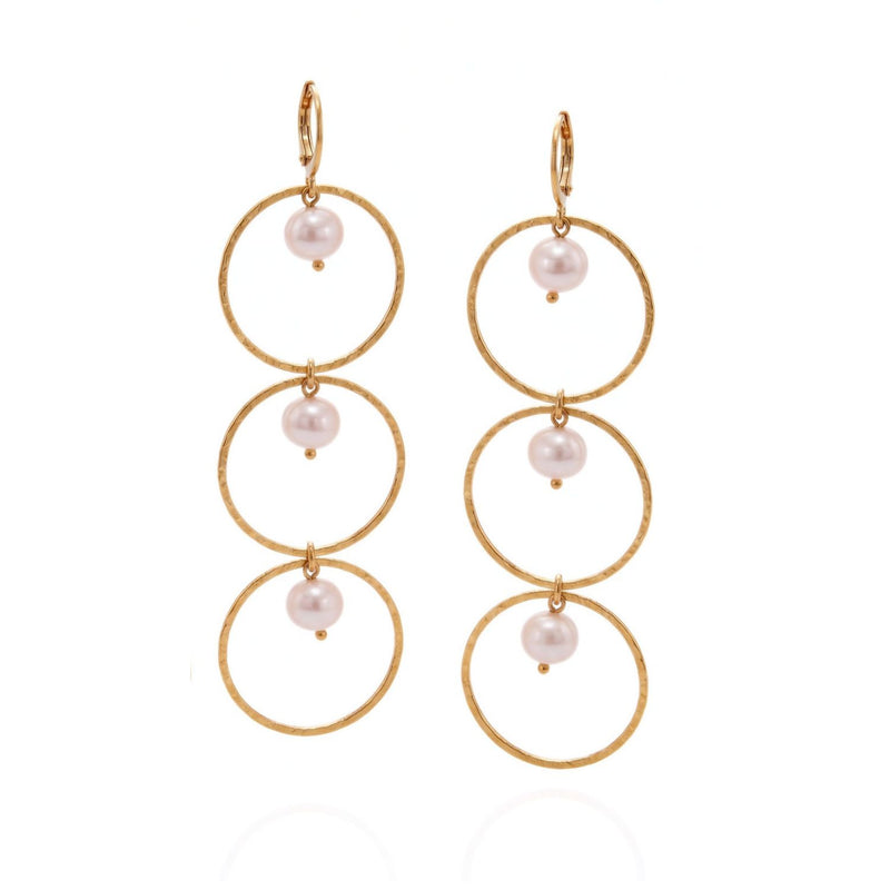 Pair of gold dangle earrings, each with three stacked thin hammered hoops joined by small white freshwater pearls, leverback hooks, side by side on a light gray background.